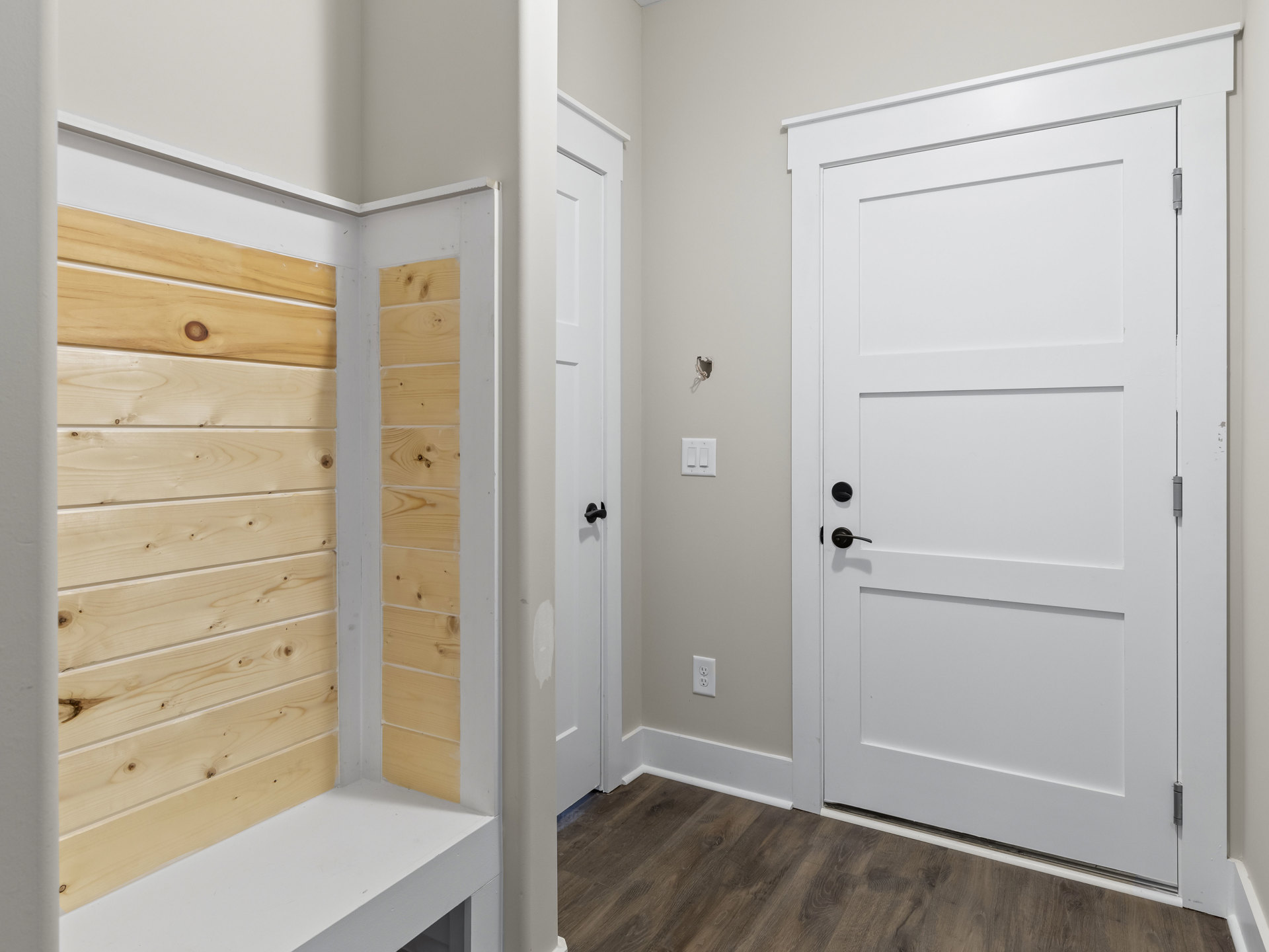 Hallway featuring white doors with black handles, wood paneled walls with white trim, wood flooring with white baseboards, and cabinetry with wood and white finishes