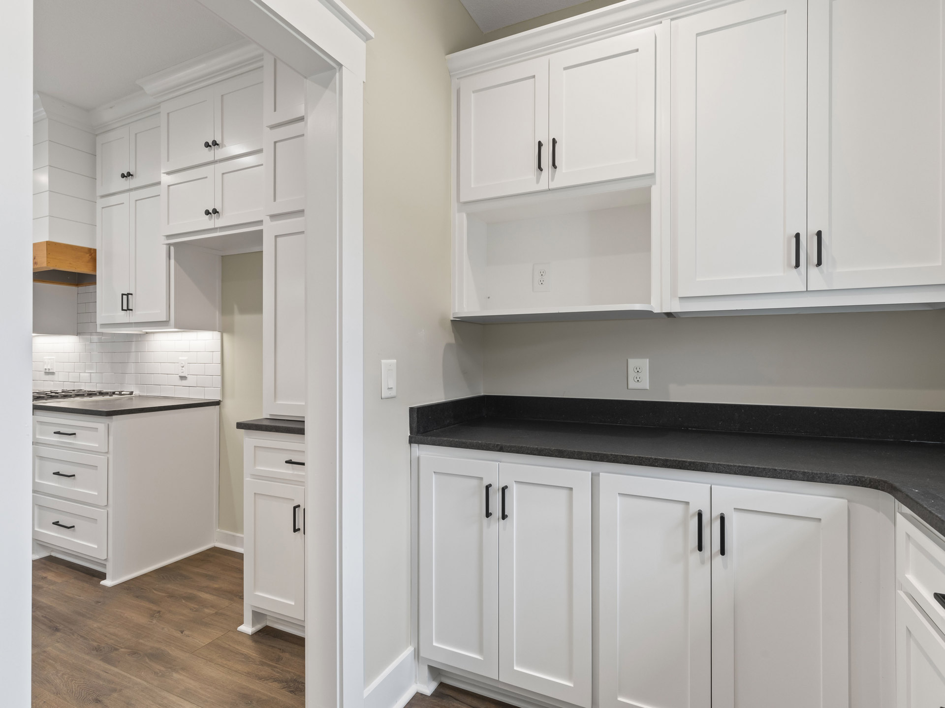 White kitchen featuring white cabinets with black handles, black countertops, white tile backsplash, and stainless steel appliances.