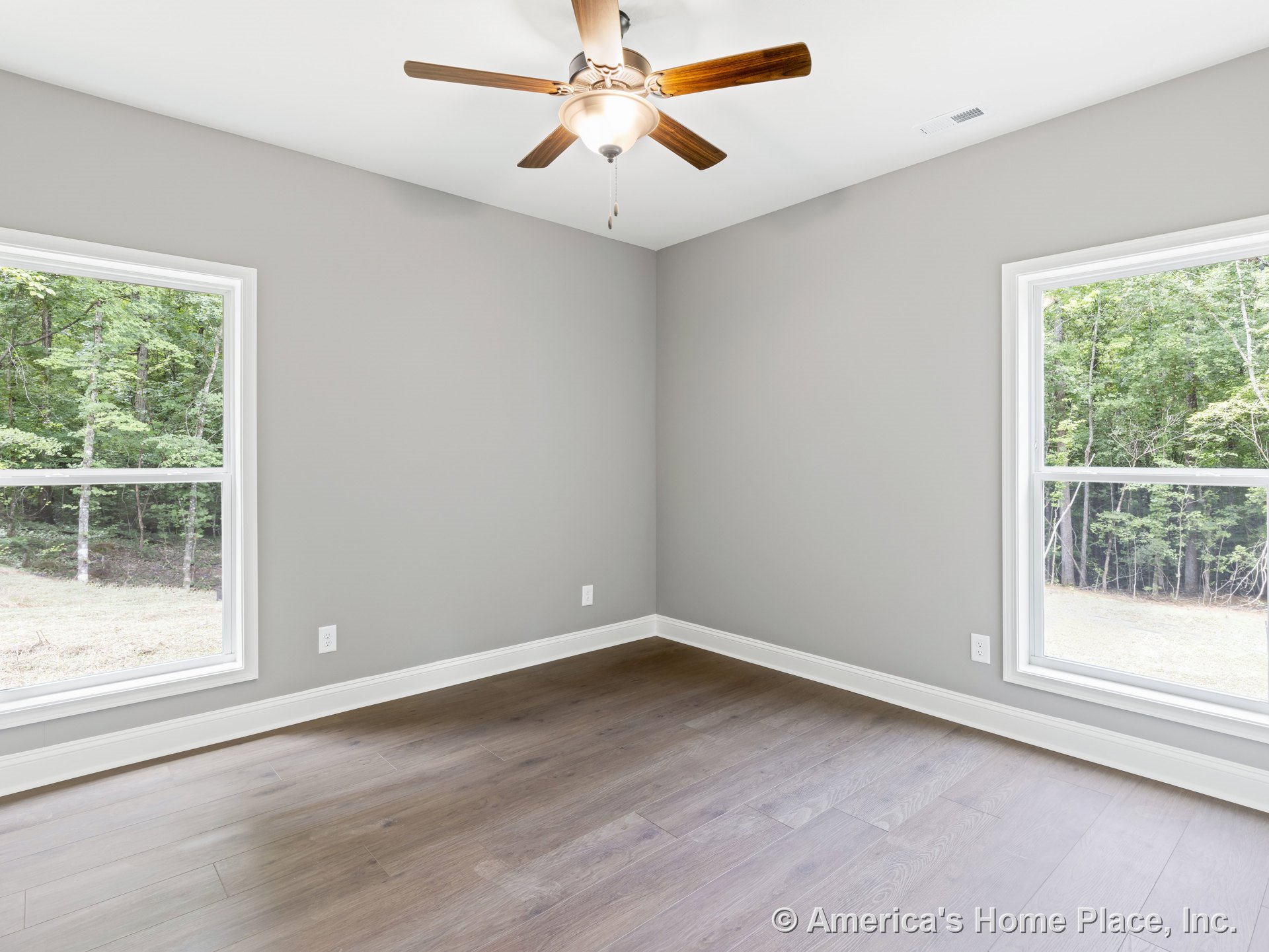 Bedroom with gray walls, white trim and baseboards, wood plank flooring, double large windows allowing natural light, and a ceiling fan with integrated light fixture.