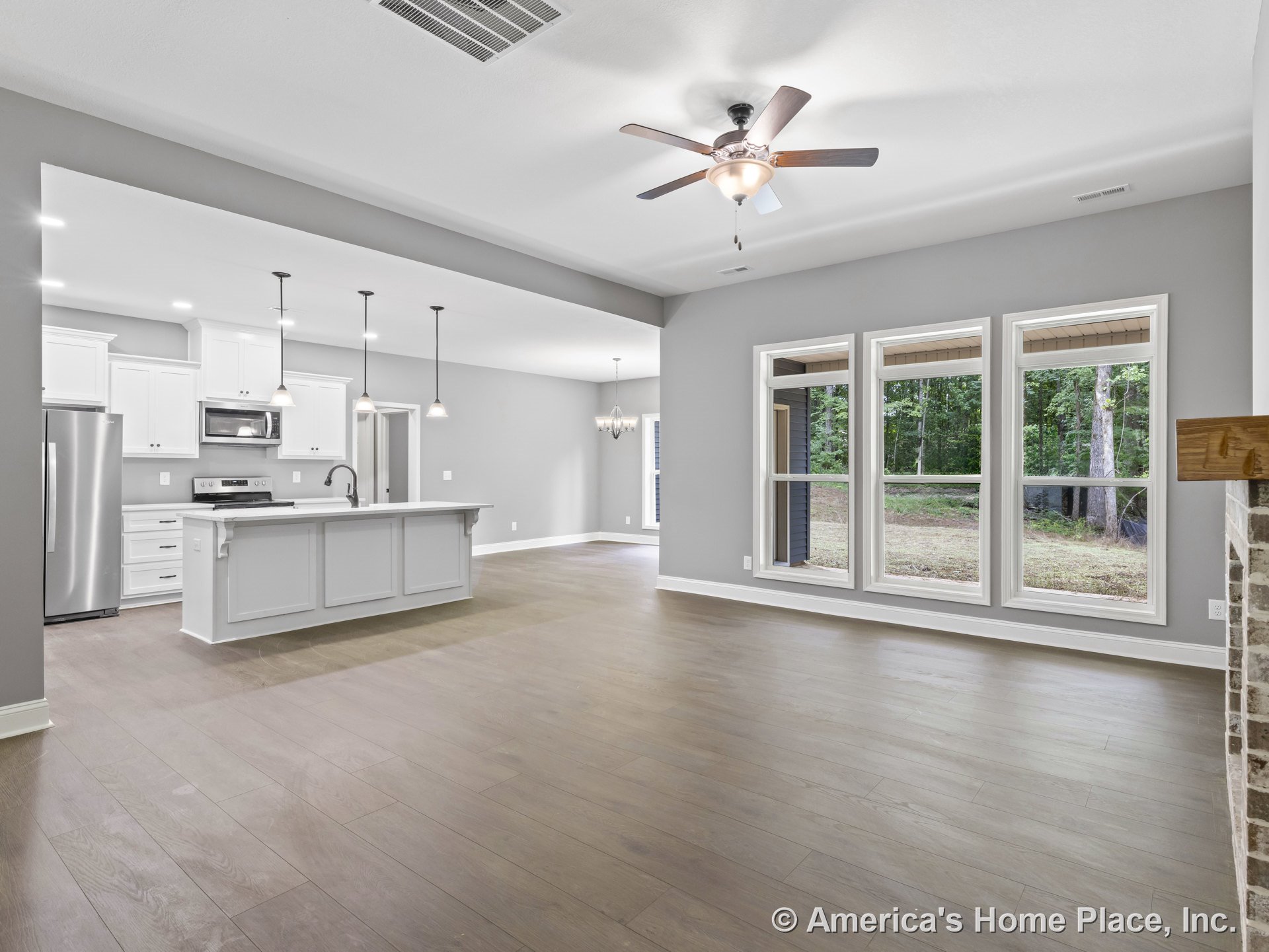 Open concept living area with expansive picture windows, wood plank flooring, modern kitchen featuring white cabinetry, stainless steel appliances, pendant lights above island