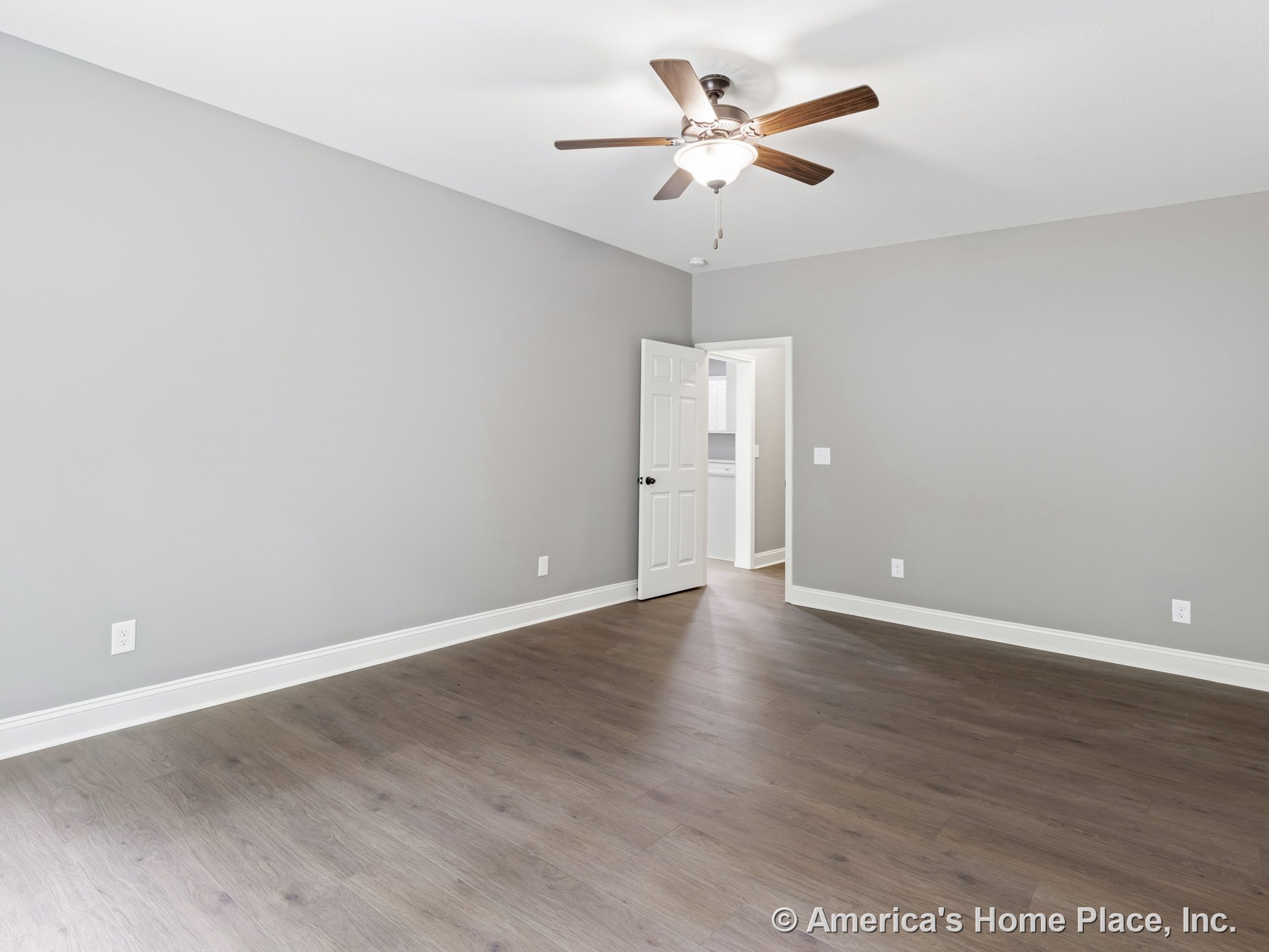 Bedroom with wood-look plank flooring, gray painted walls, white baseboard trim, ceiling fan and integrated light fixture, white paneled door, and visible electrical outlets.
