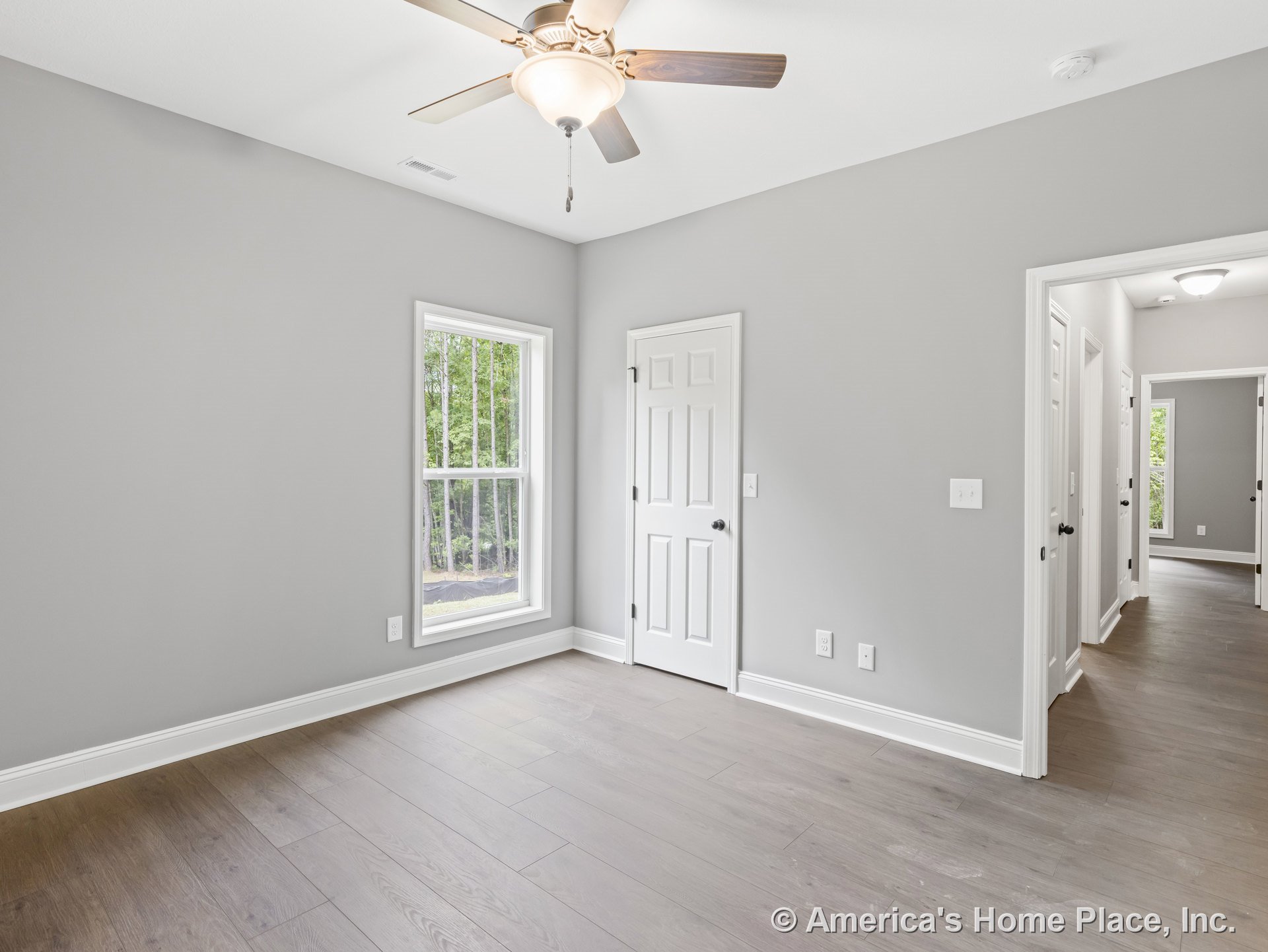 Bedroom with light gray walls, wide plank wood flooring, double-hung window, white interior doors, ceiling fan with built-in lighting, white baseboards, and modern neutral