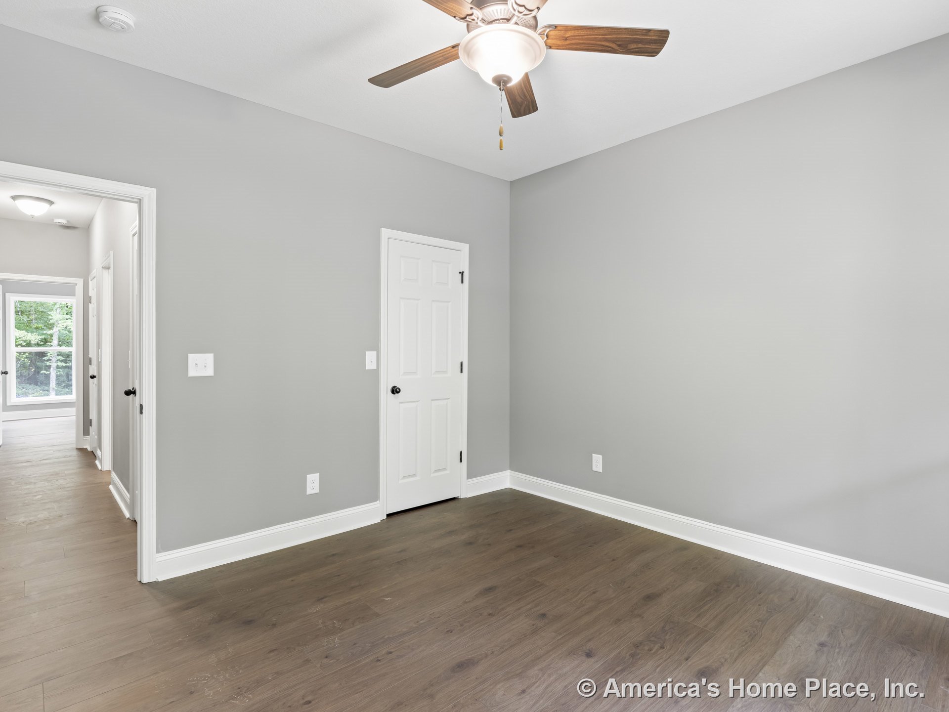 Bedroom with wood-look plank flooring, gray painted walls, white trim and baseboards, ceiling fan with integrated light, white paneled interior doors, and natural light entering