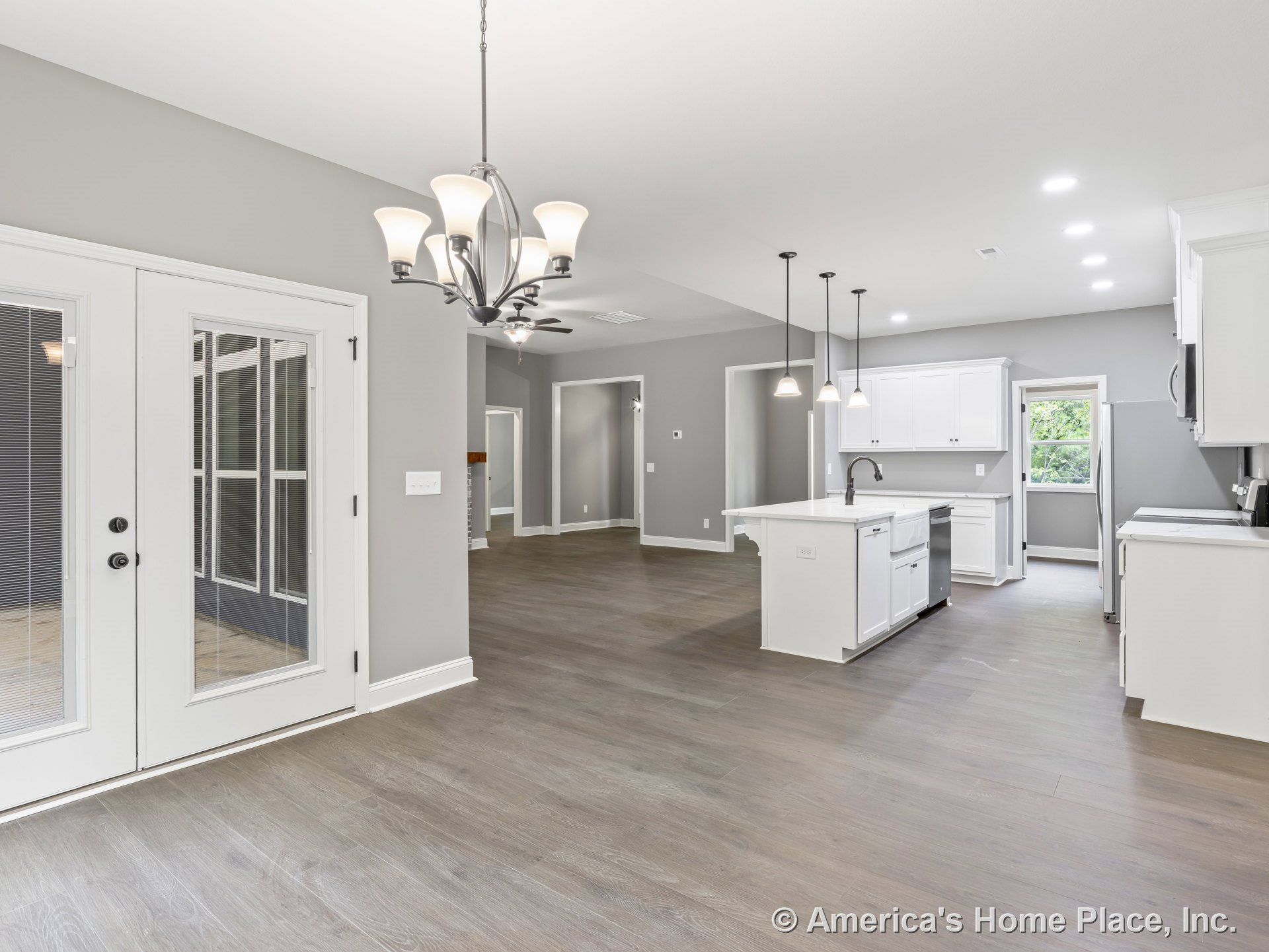 Open kitchen and dining area with white shaker cabinets, large island featuring built-in sink, pendant lights above island, recessed ceiling lights, wide plank wood flooring, and