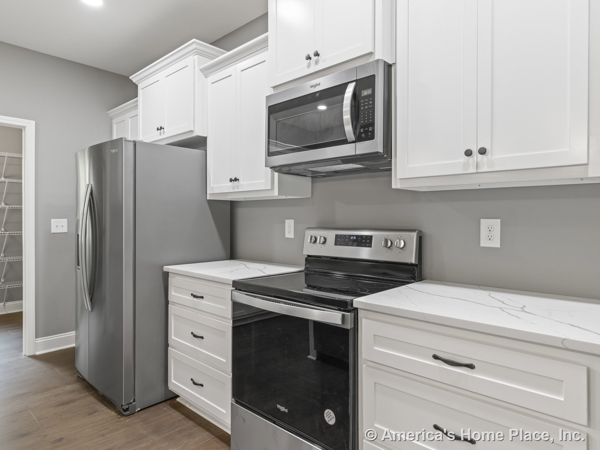 White shaker cabinets with brushed metal hardware, marble-patterned countertops, stainless steel refrigerator, built-in microwave above electric range, gray painted walls