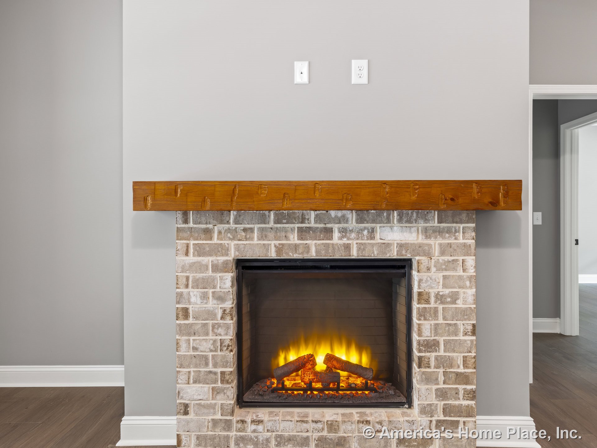 Brick fireplace with wood mantel and electric insert built into gray painted living room wall, white baseboard trim, and hardwood flooring.