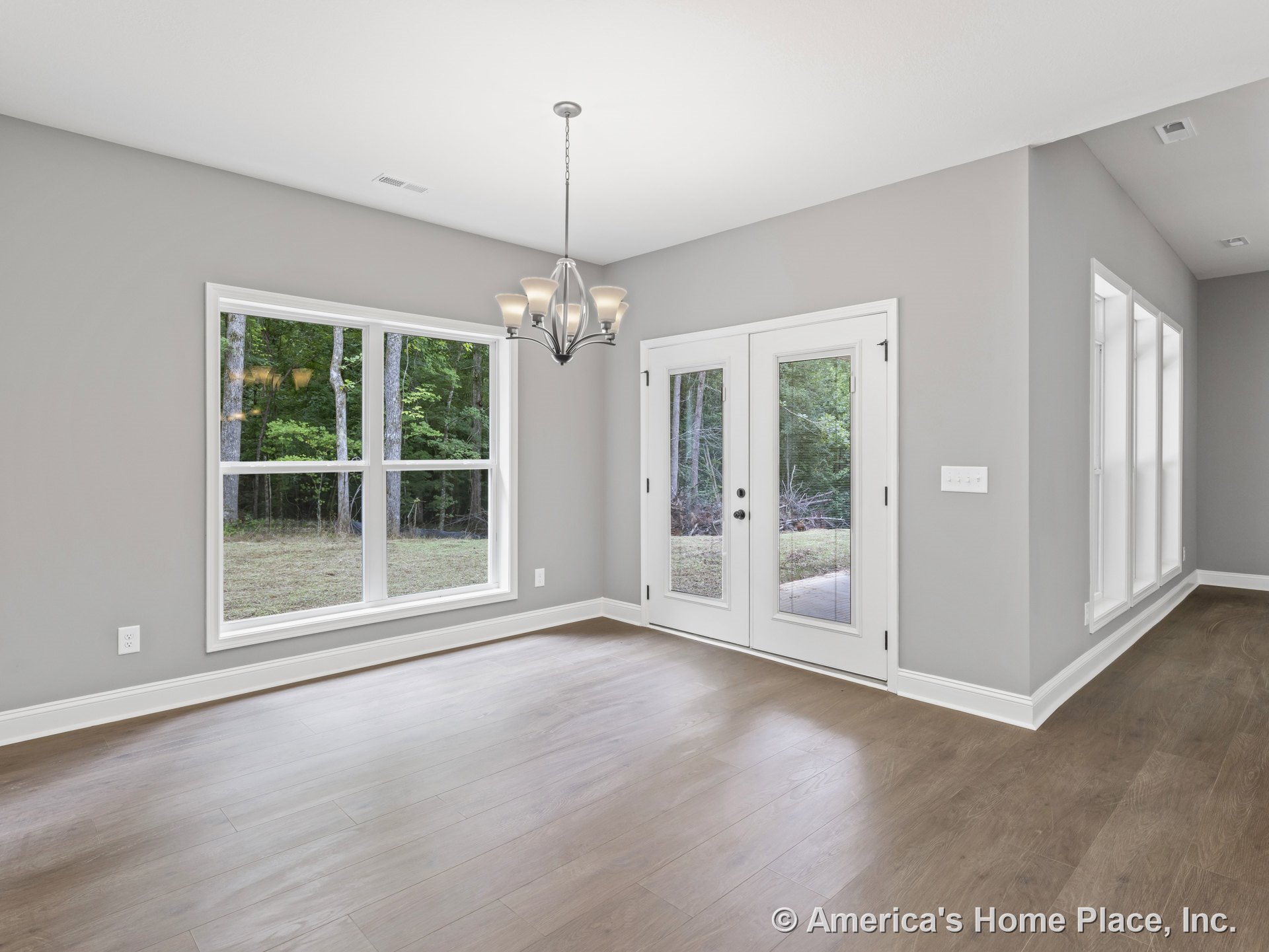 Dining area with large double window, French doors with glass panels, modern chandelier, wood-look plank flooring, gray painted walls, and white baseboard trim.