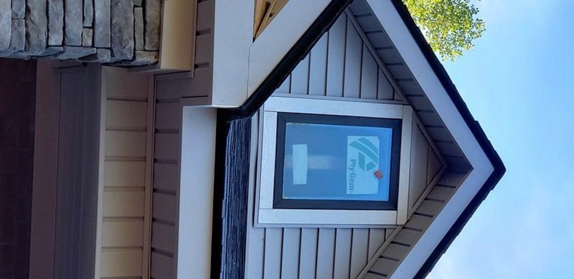 Small house exterior with white wall, stone accents, single window, and tree with green leaves in foreground