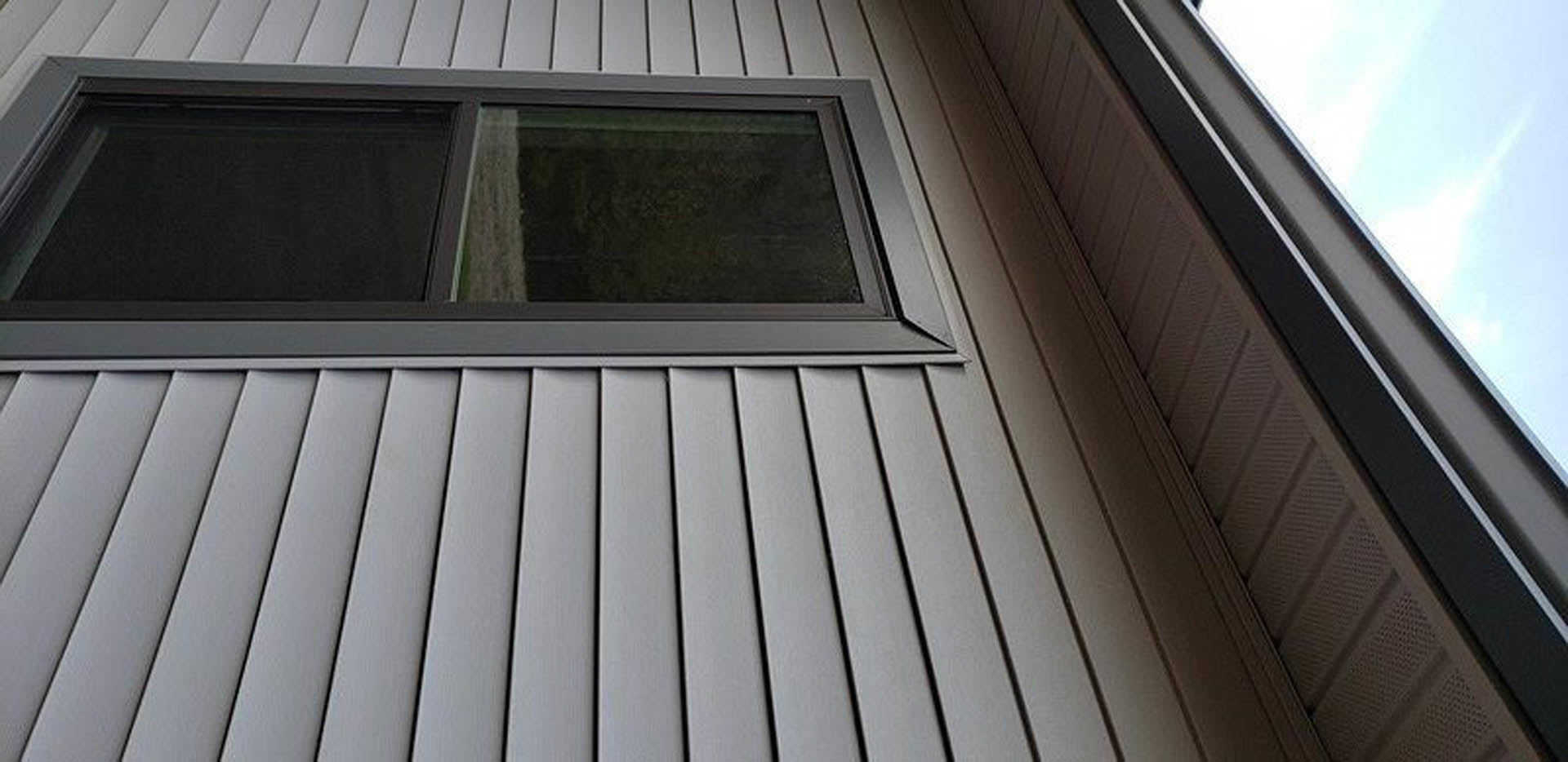 Black-framed rectangular window set into a dark metal roof, reflecting blue sky, surrounded by smooth black roofing panels.