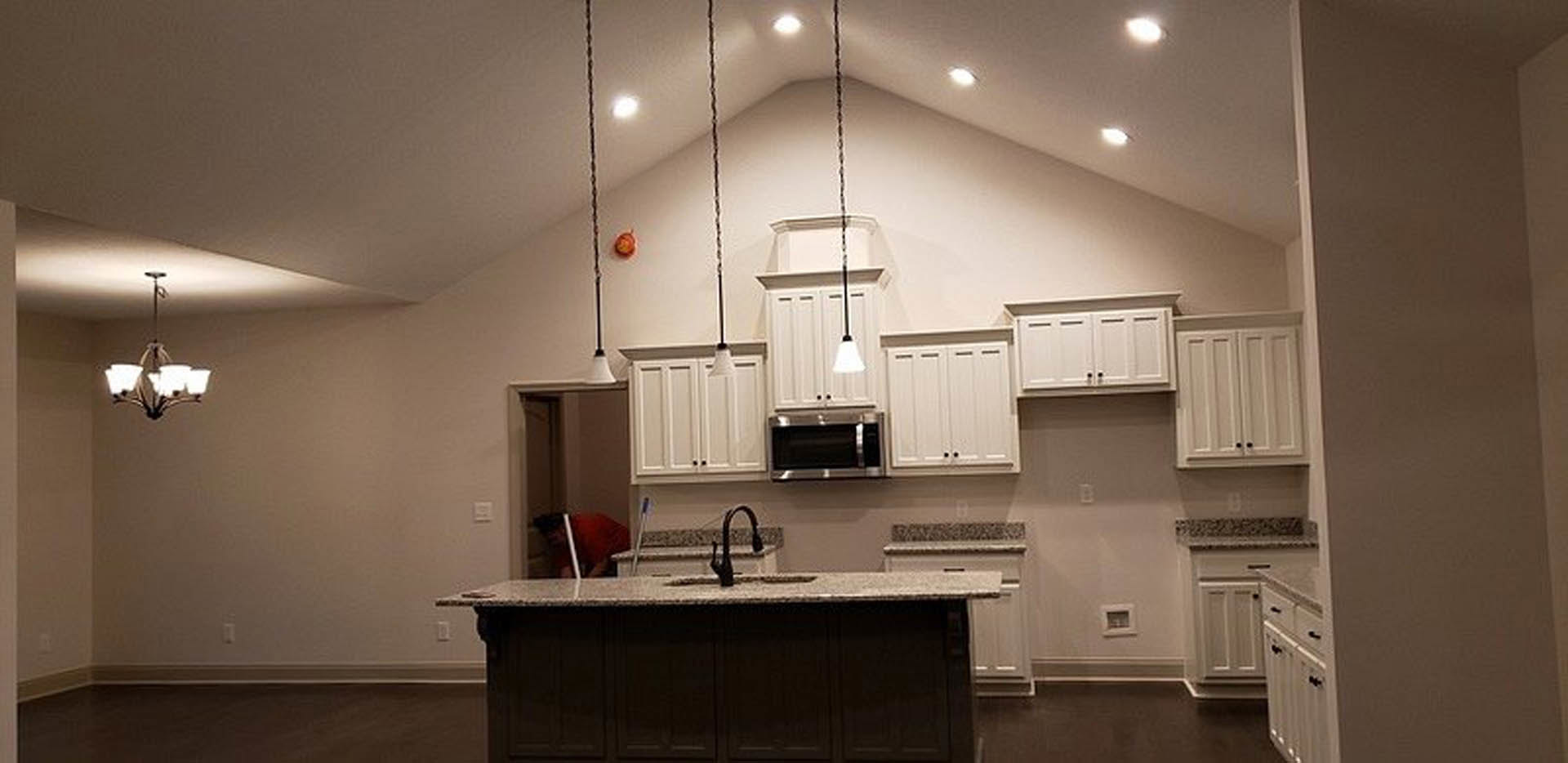 Spacious kitchen featuring a large central island with white quartz countertop, dark wood cabinetry, stainless steel sink and faucet, pendant bell light fixtures, and small square