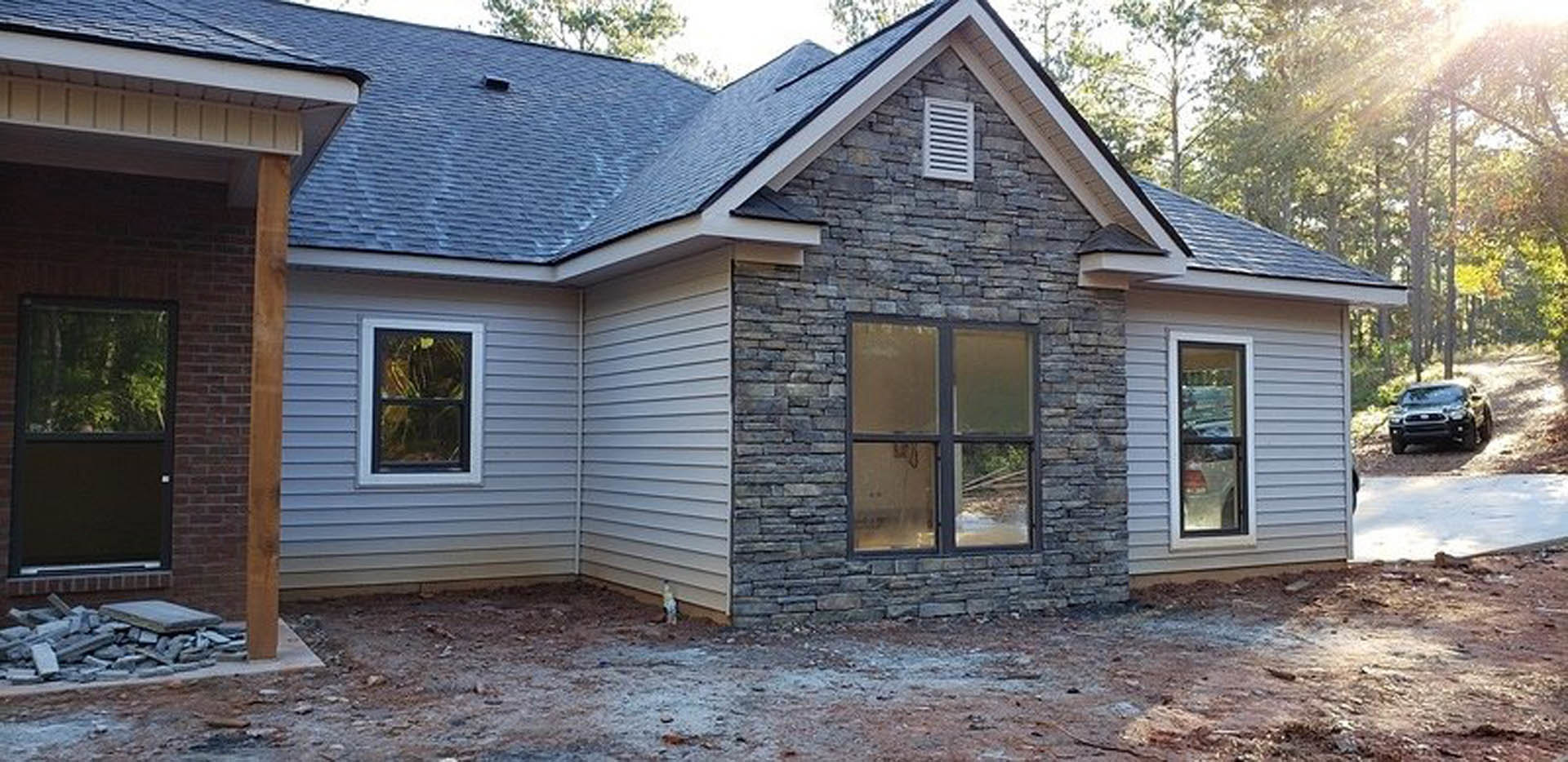 Red brick exterior wall with black-framed window, trees reflected in glass, black car parked on street, cloudy sky overhead