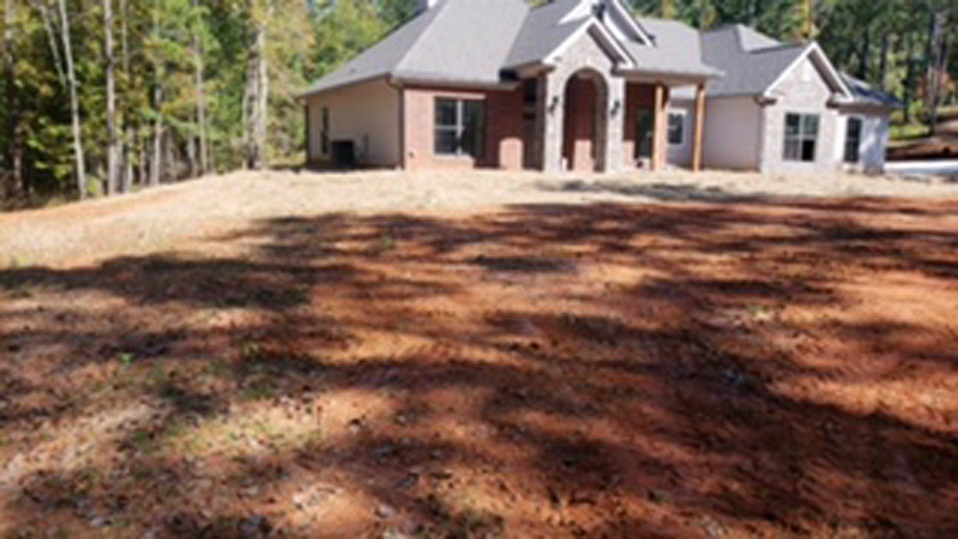 Modern farmhouse with white siding, large windows, and a dirt yard shaded by trees