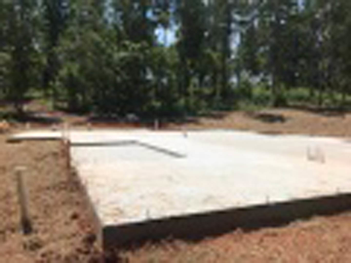 Concrete foundation slab set in a dirt lot with trees in the background
