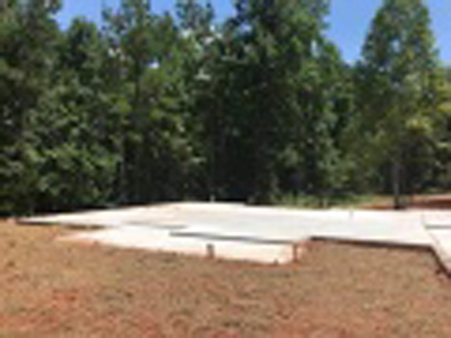 Concrete foundation slab set in grassy field with mature trees in background