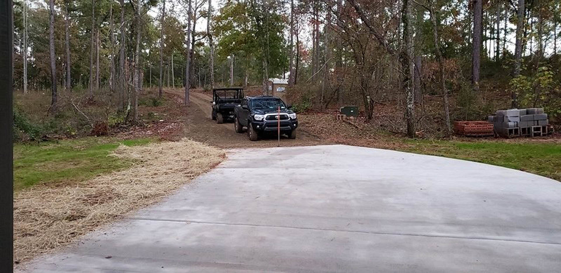 Black pickup truck parked on dirt road beside grassy area with trees in background
