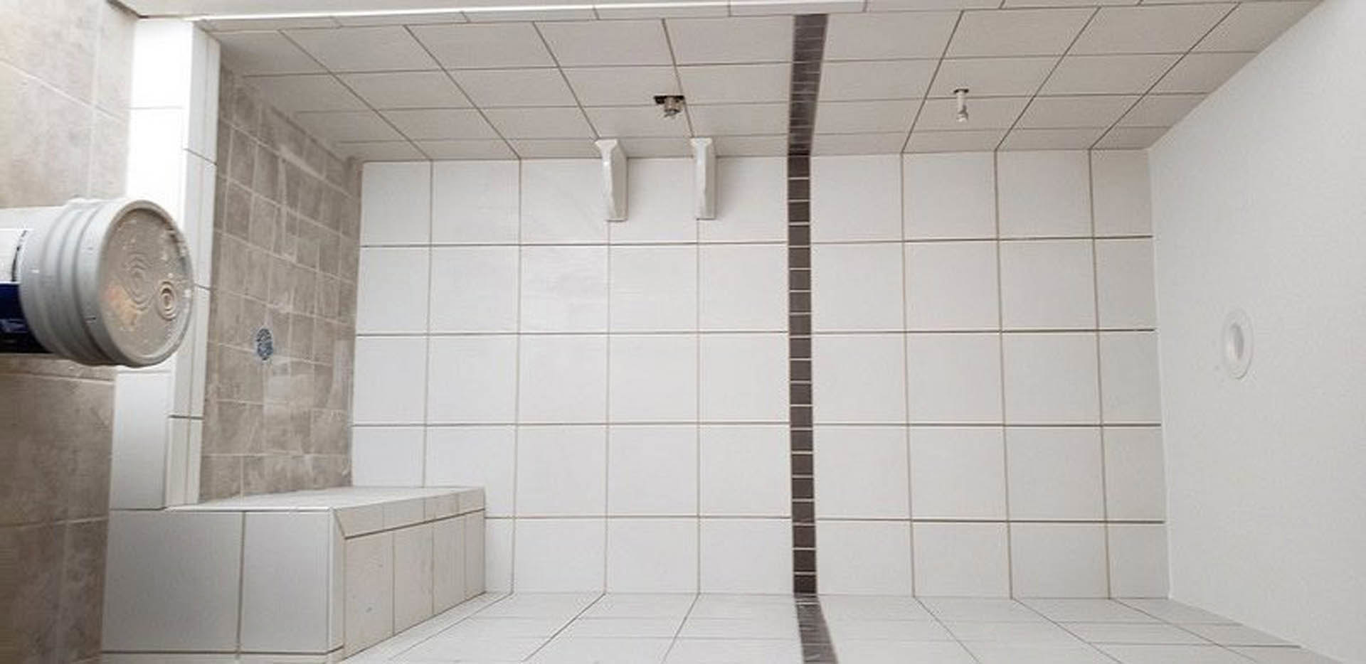 White tiled bathroom featuring a built-in bathtub, black grout lines, white cabinetry with drawers, and a window providing natural light.