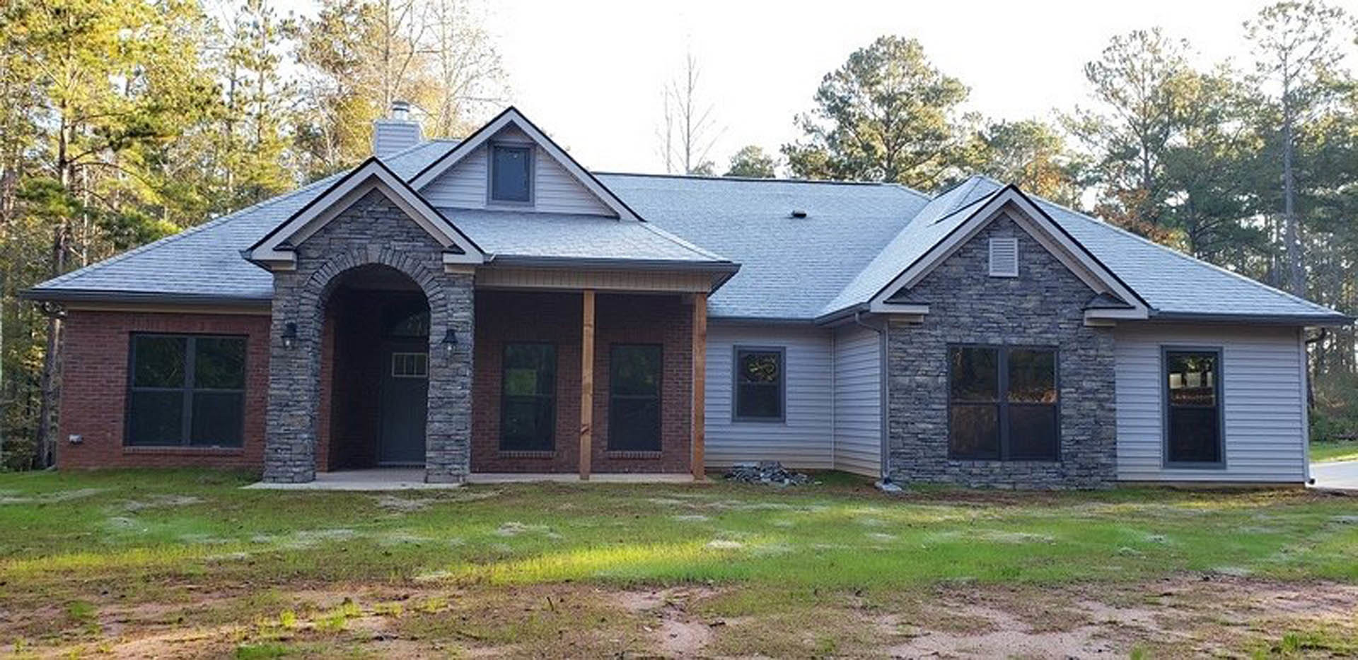 Modern custom home with white siding, black-framed windows, covered porch, dark entry door with glass panel, manicured green lawn, and mature trees in the yard.