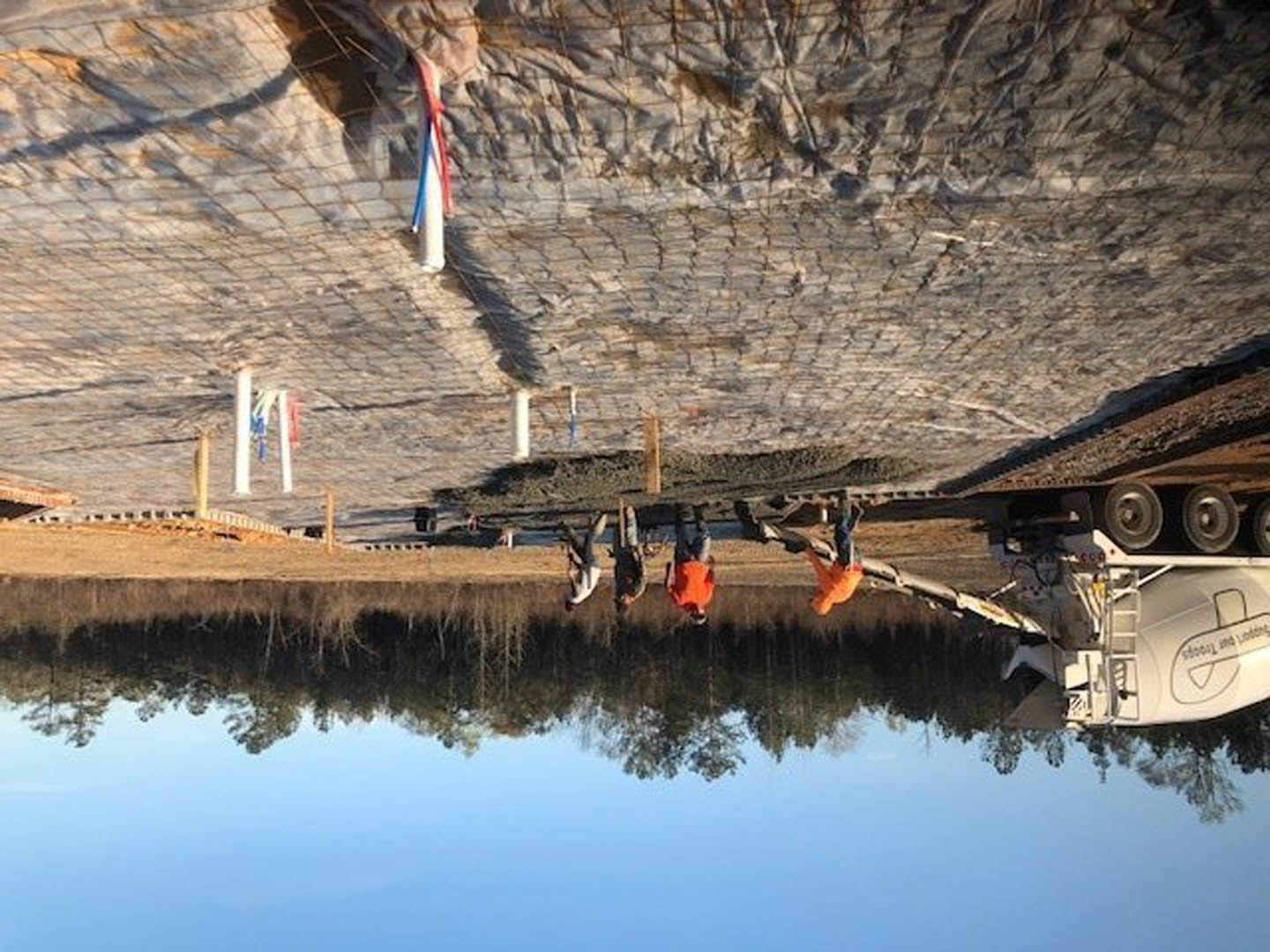 Modern lakeside home with wood siding, large windows, and stone accents nestled among trees, reflecting on calm water.
