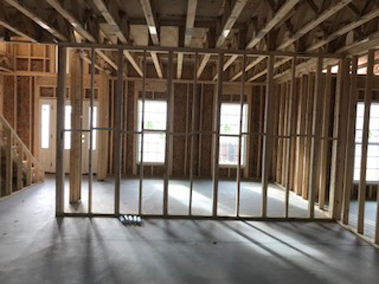 Bright room with wood plank flooring, white-framed windows, exposed ceiling beams, and scattered objects on the floor.