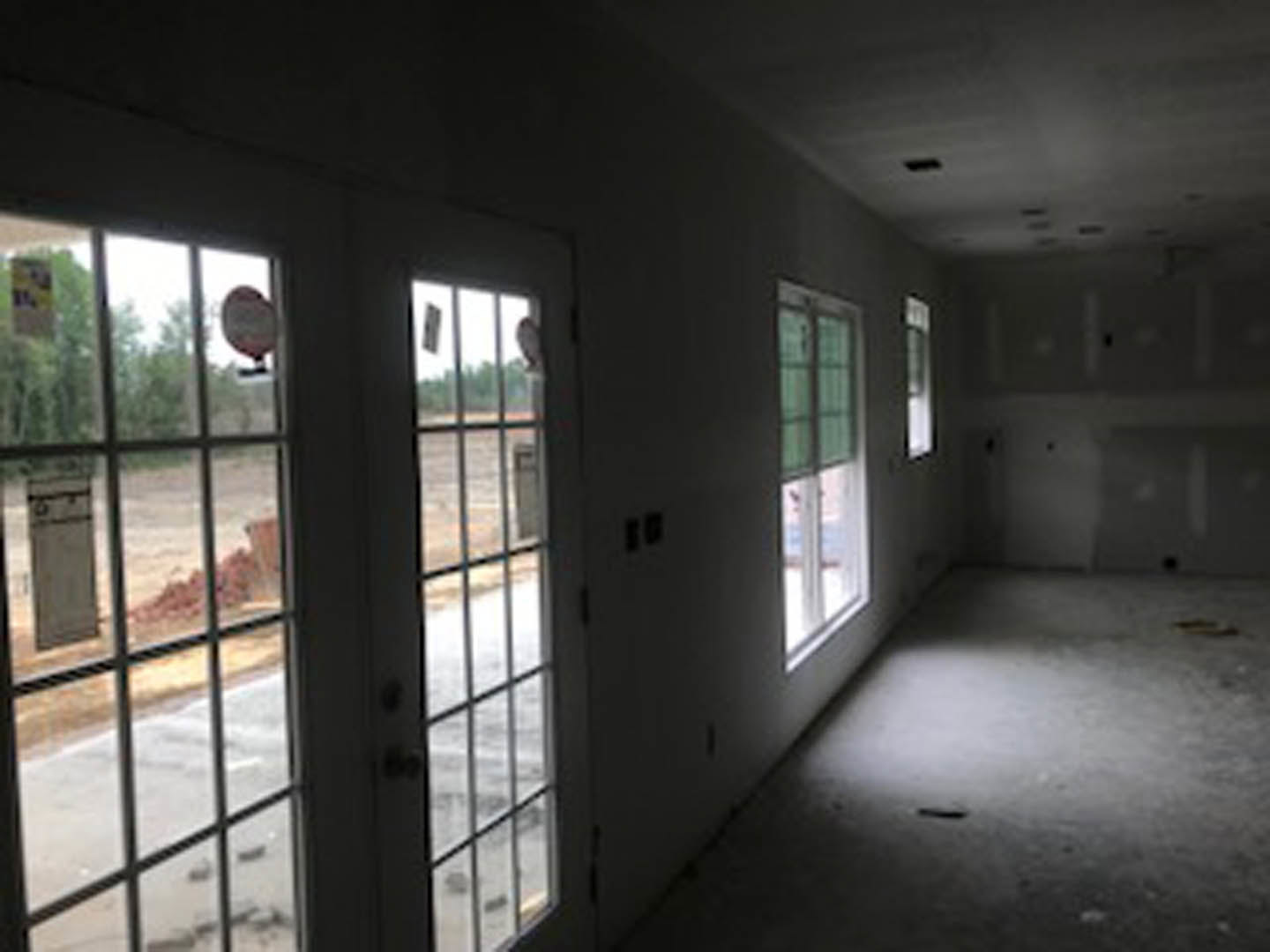 Wide hallway with light wood flooring, white walls, and double glass-paneled doors; large windows line one side, allowing natural daylight to fill the space.