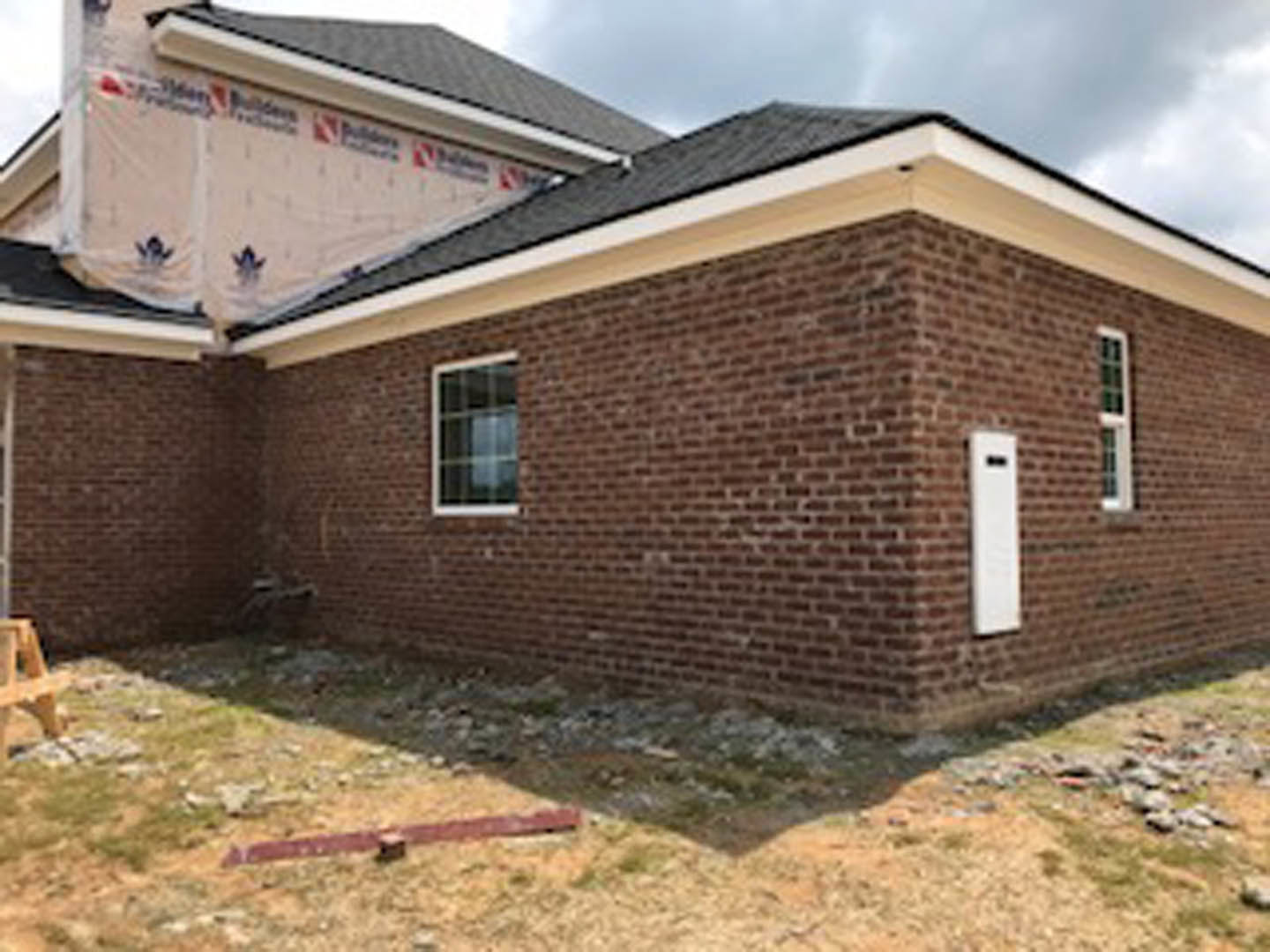 Red brick exterior with white-framed window, gabled roof, and cloudy sky backdrop