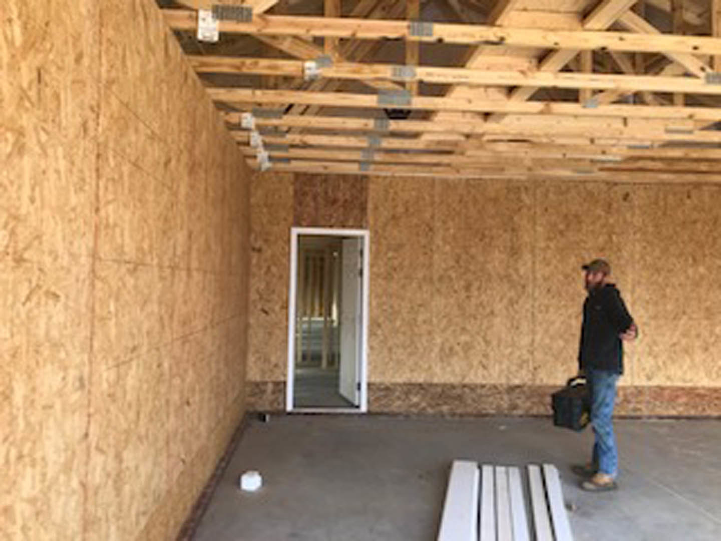 Man holding toolbox in unfinished room with exposed wooden beams, white ceiling, and barred window