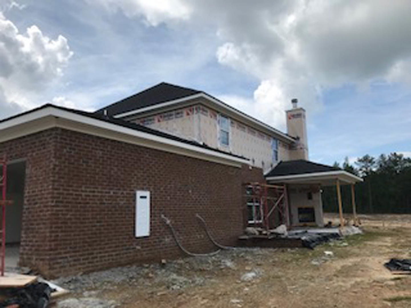 Red brick house with black roof, two chimneys, white-framed window, cloudy sky overhead