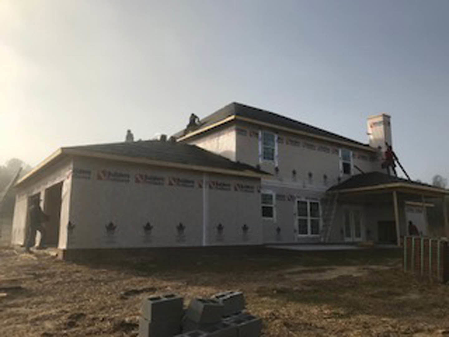 Two-story cottage with gabled roof, brick chimney, white siding, and large windows surrounded by green lawn under partly cloudy sky