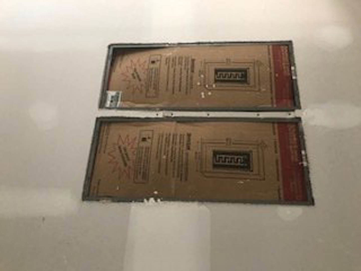 Pair of cardboard moving boxes resting on a white floor with black trim, adjacent to a plain white wall in a residential interior.