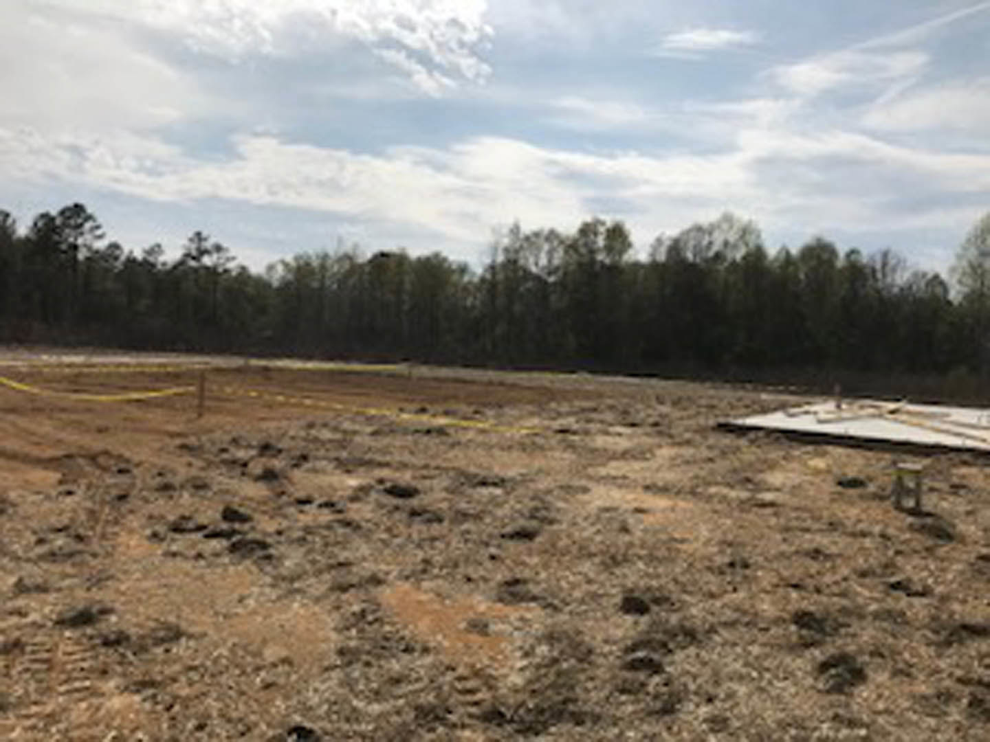 Dirt field bordered by trees under a partly cloudy blue sky
