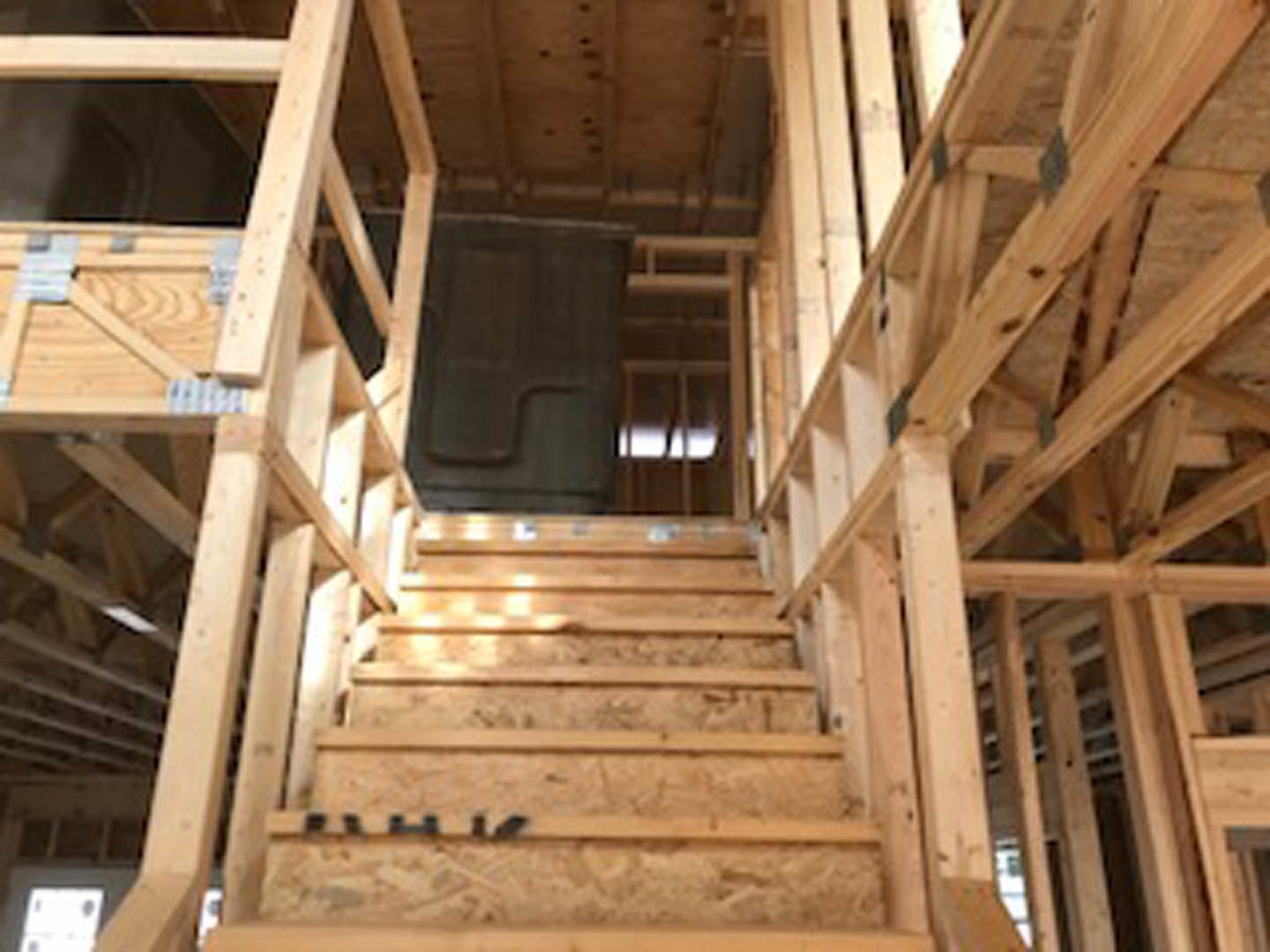 Wooden staircase with natural hardwood treads and vertical wooden posts, set in a modern interior with exposed beams and plank ceiling