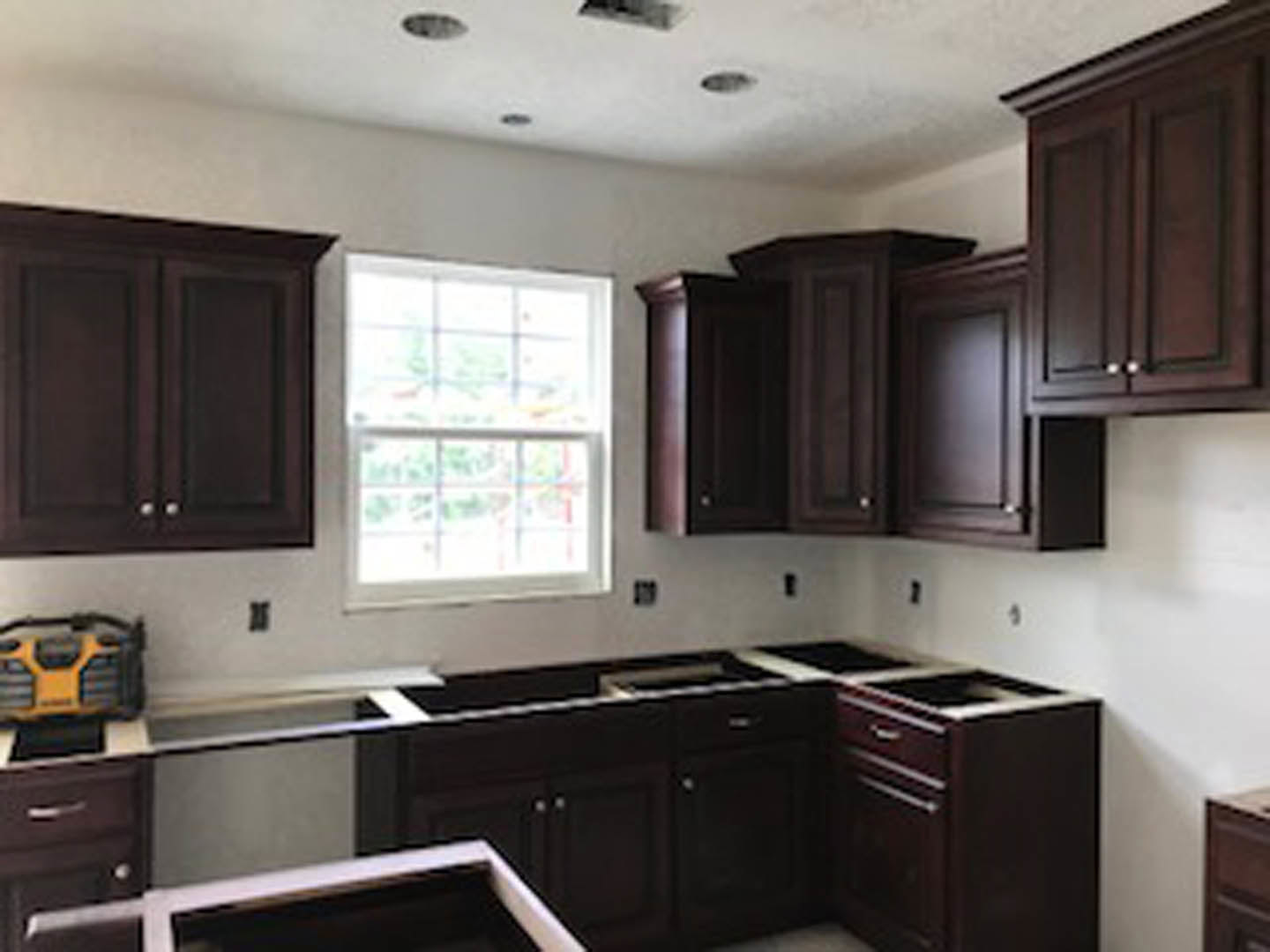 Kitchen with dark wood cabinets, stone countertops, stainless steel appliances, square-paned window, and a close-up of a yellow and black device on the table