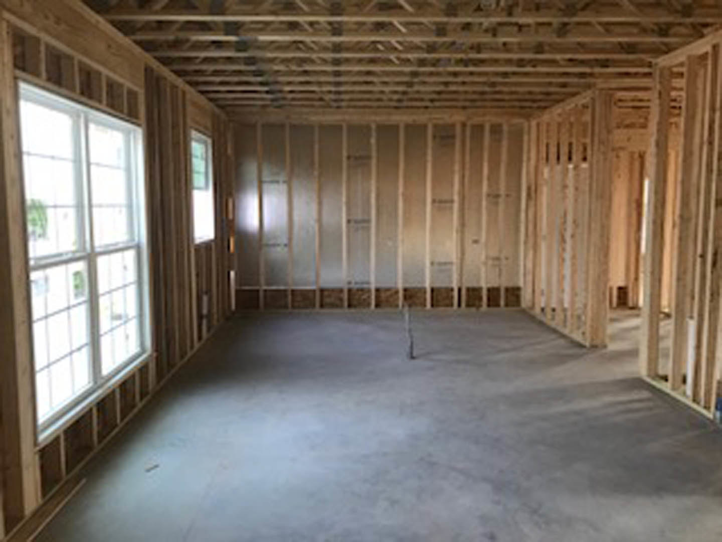 Concrete floor with exposed metal rod, large windows framed by wood, glass wall panels, and visible wooden beams and ceiling structure