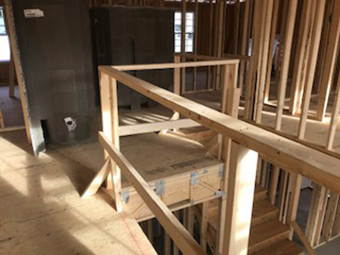 Exposed wood framing and beams with unfinished plywood flooring, partially constructed wooden staircase, multiple windows letting in natural light