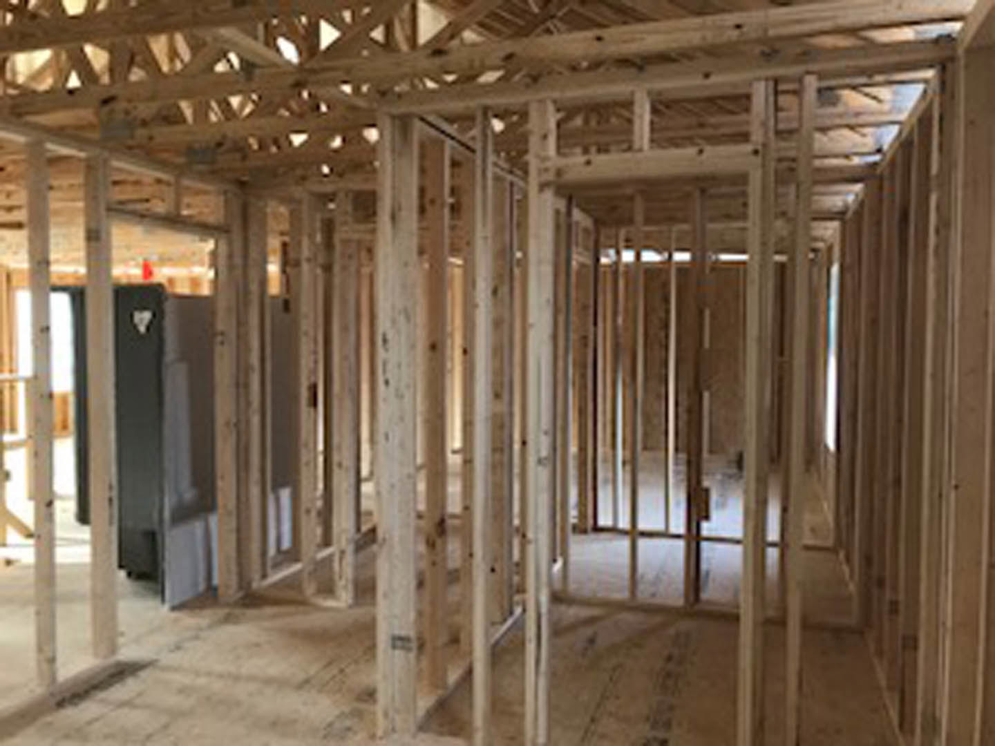Exposed wooden framing and beams inside a partially constructed home, with unfinished walls and ceiling, visible insulation, and a concrete floor.