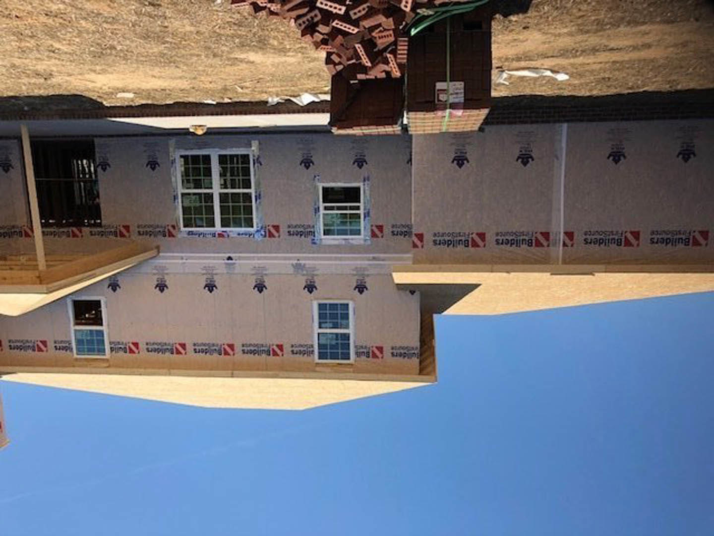 Framed house under construction beneath clear blue sky, featuring white-trimmed windows and exposed wooden structure