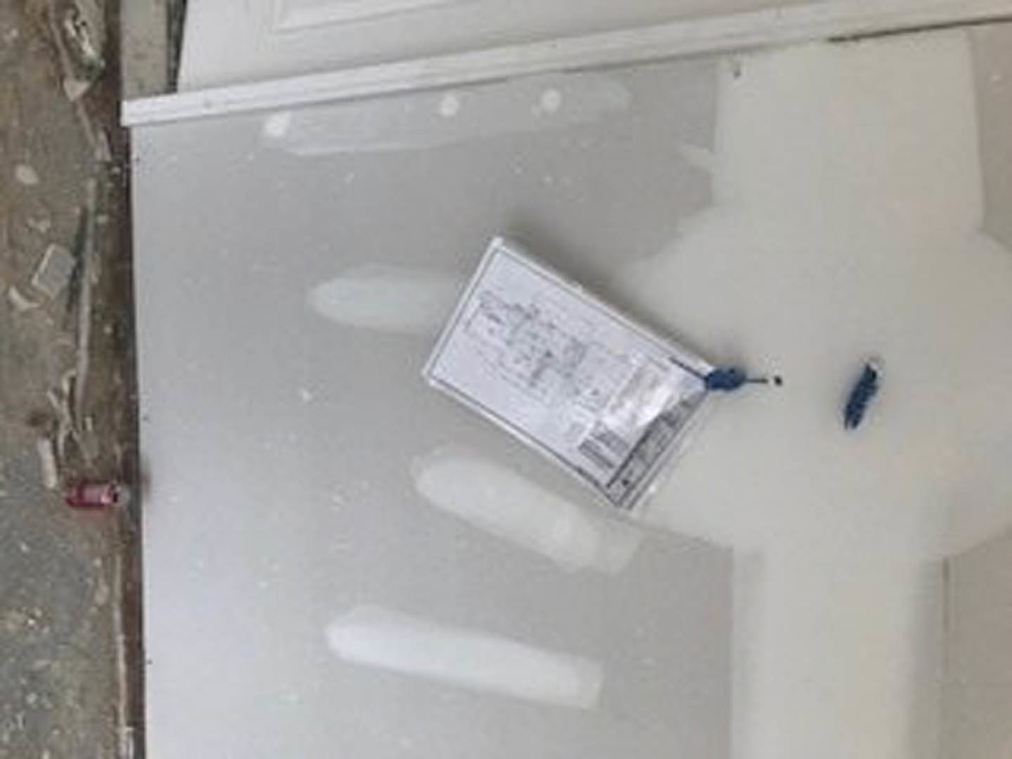 White kitchen interior with a white refrigerator, stainless steel sink, and a white board on the counter holding a blue screwdriver and a piece of paper.