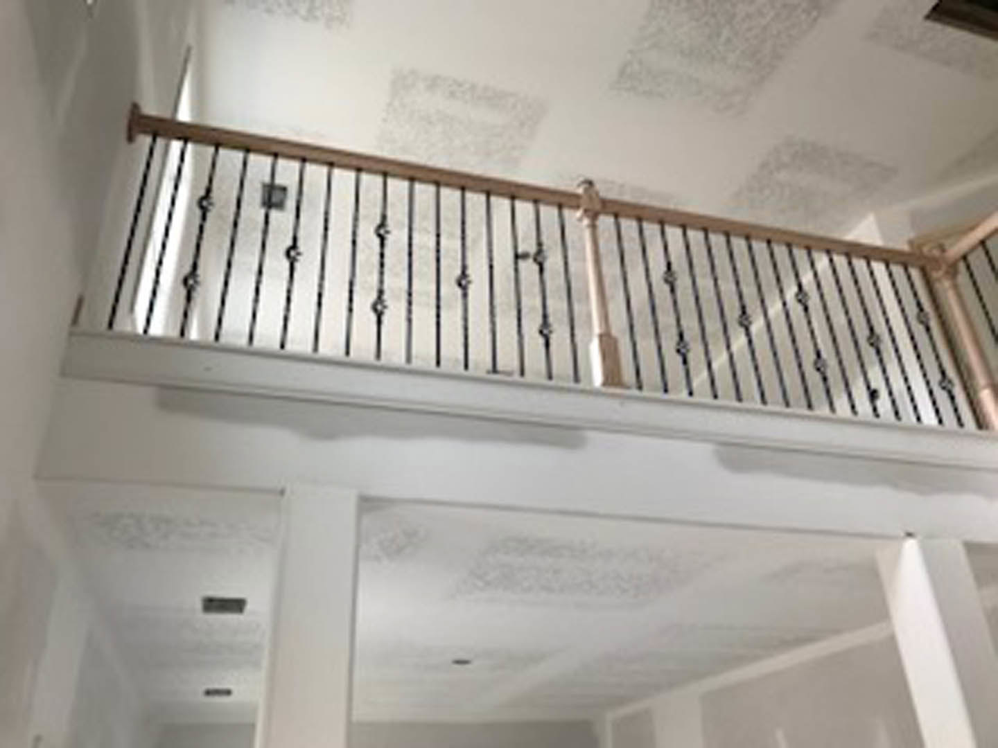 White staircase with sleek metal railing in a bright room, plaster walls and ceiling with recessed opening visible above.