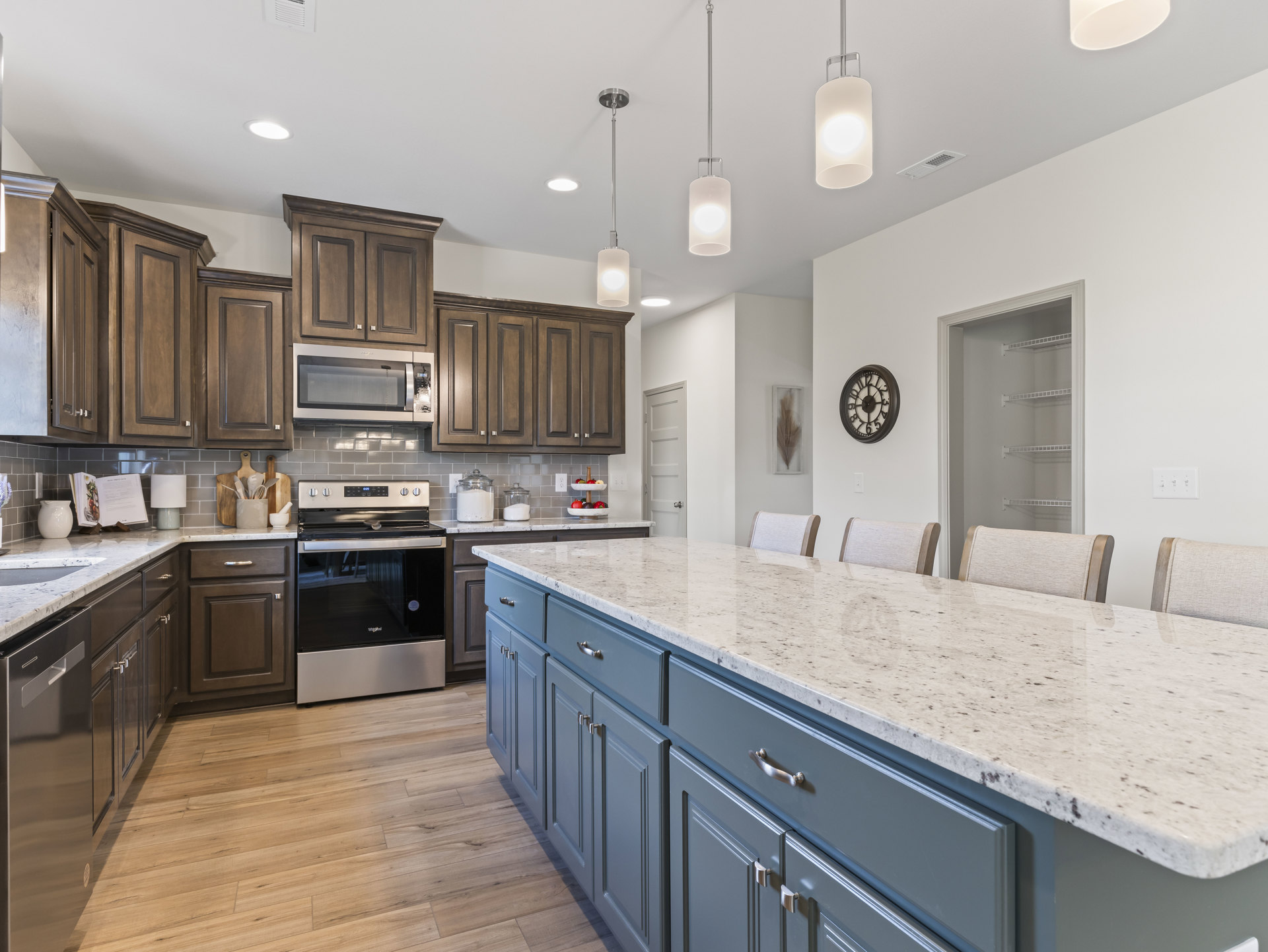 Spacious kitchen featuring a large central island with bar chairs, white cabinetry, stainless steel appliances including a black and silver stove and built-in microwave, wall