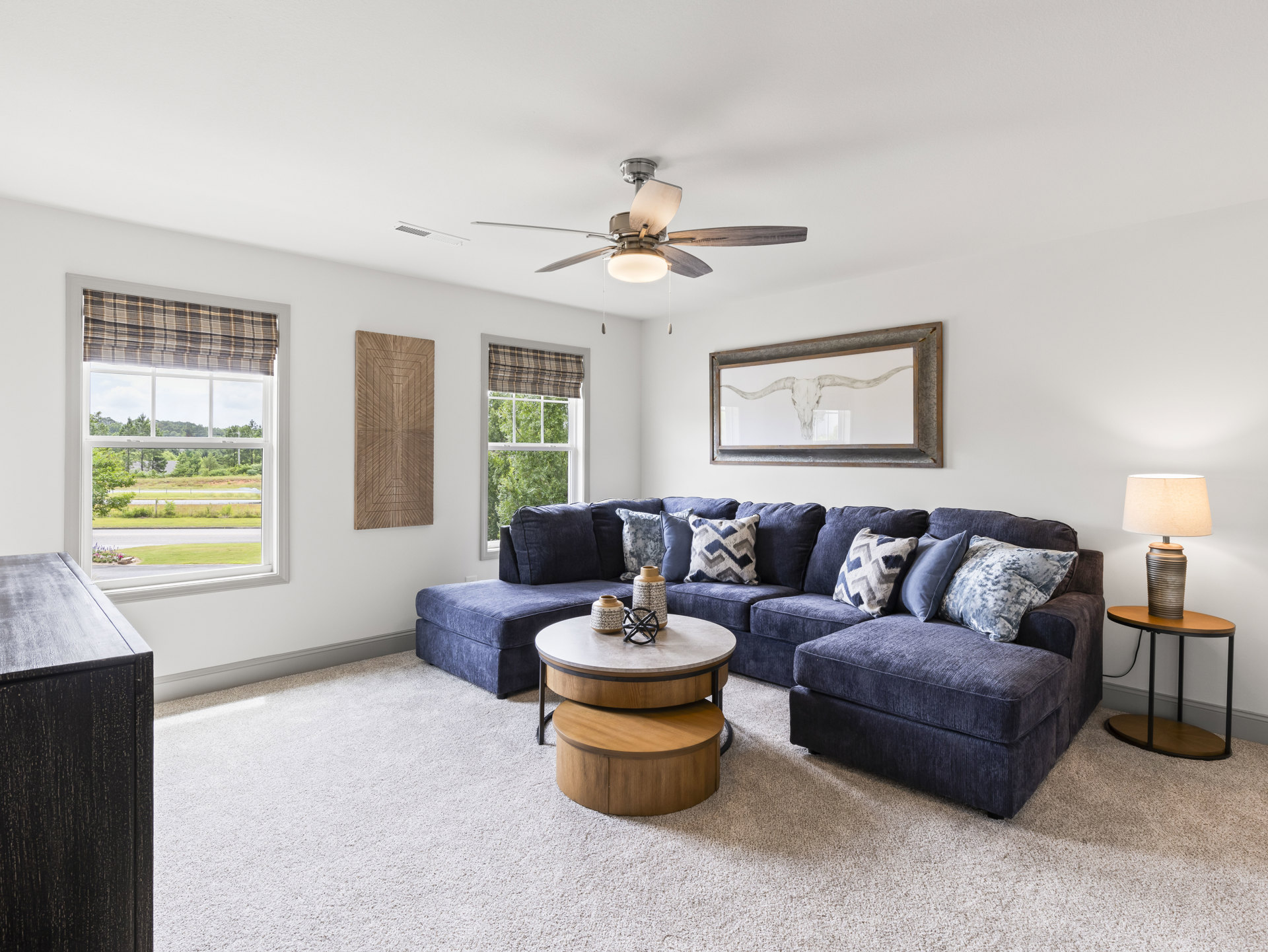Living room with light gray couch, patterned pillows, wooden coffee table, ceiling fan, bull skull painting on wall, round side table with metal decor, dark wood flooring
