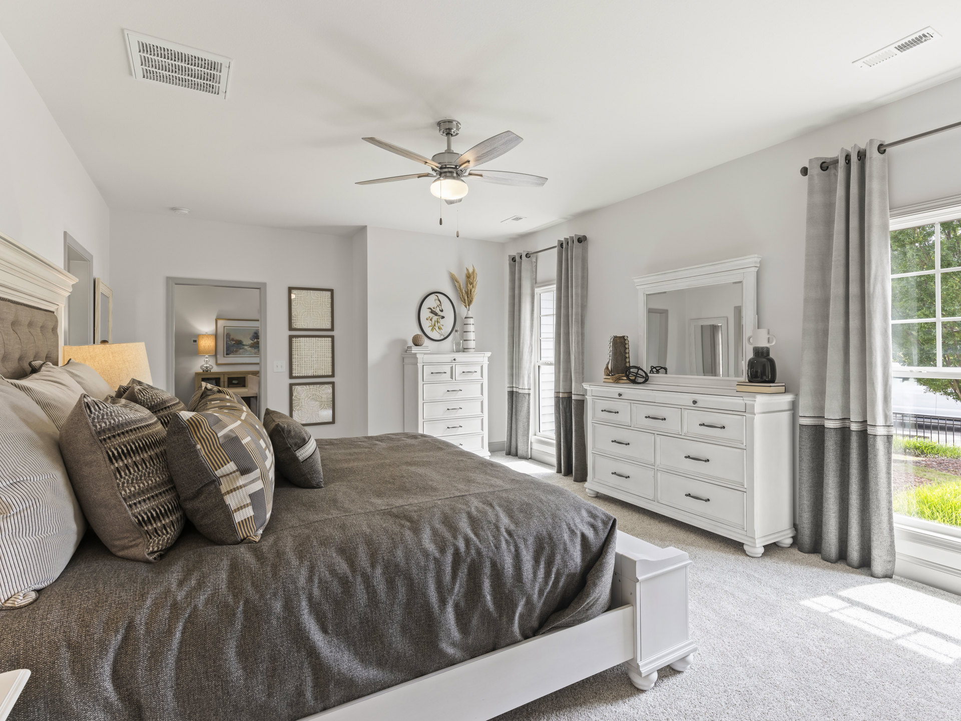 Bedroom with a white dresser topped by a mirror, bed with pillows and linens, ceiling fan with light, wall art featuring birds on a branch, and ceiling vent