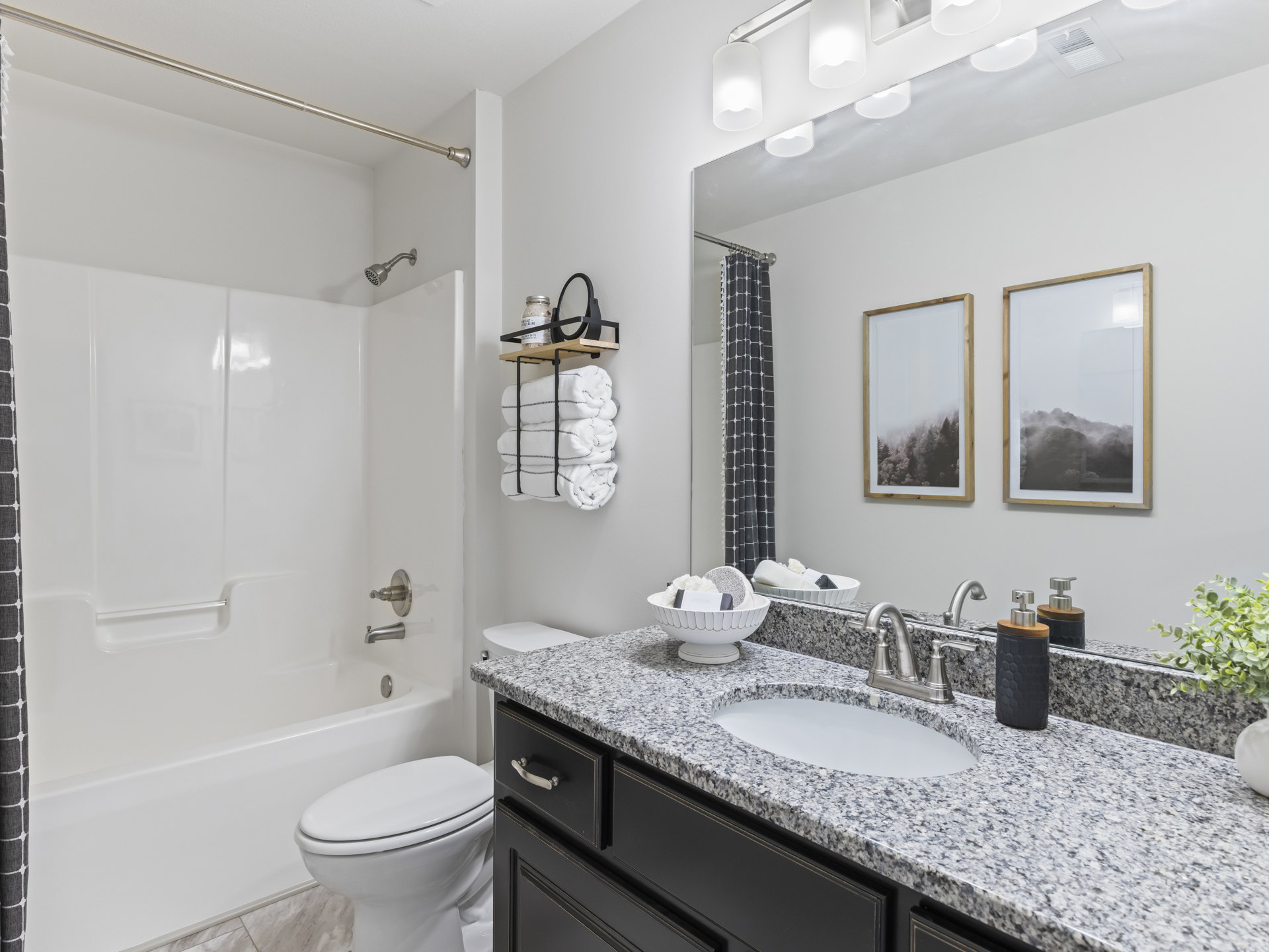 Modern bathroom featuring white ceramic sink and toilet, glass-enclosed shower with tile walls, light stone countertop, black container with wooden lid, decorative bowl, and framed