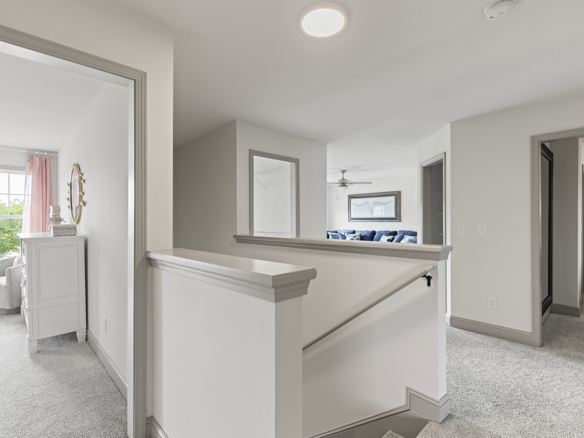 Wood staircase with white risers and railing, bull skull mounted on plaster wall, white dresser and shelf in adjacent room, recessed ceiling light above, hardwood flooring