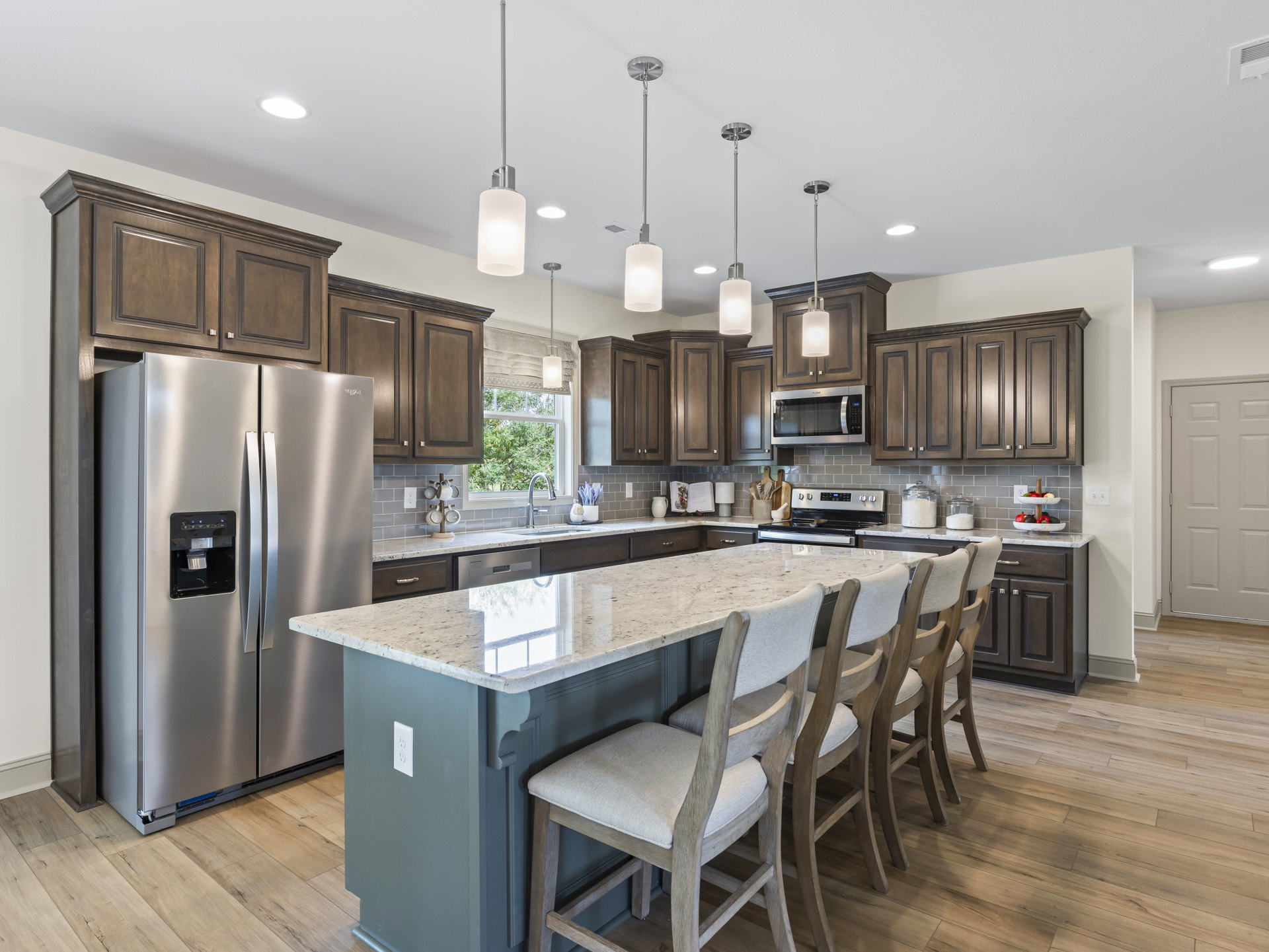 Spacious kitchen featuring a large central island with seating, stainless steel refrigerator with black handle, built-in microwave with glass door, white cabinetry, and a white
