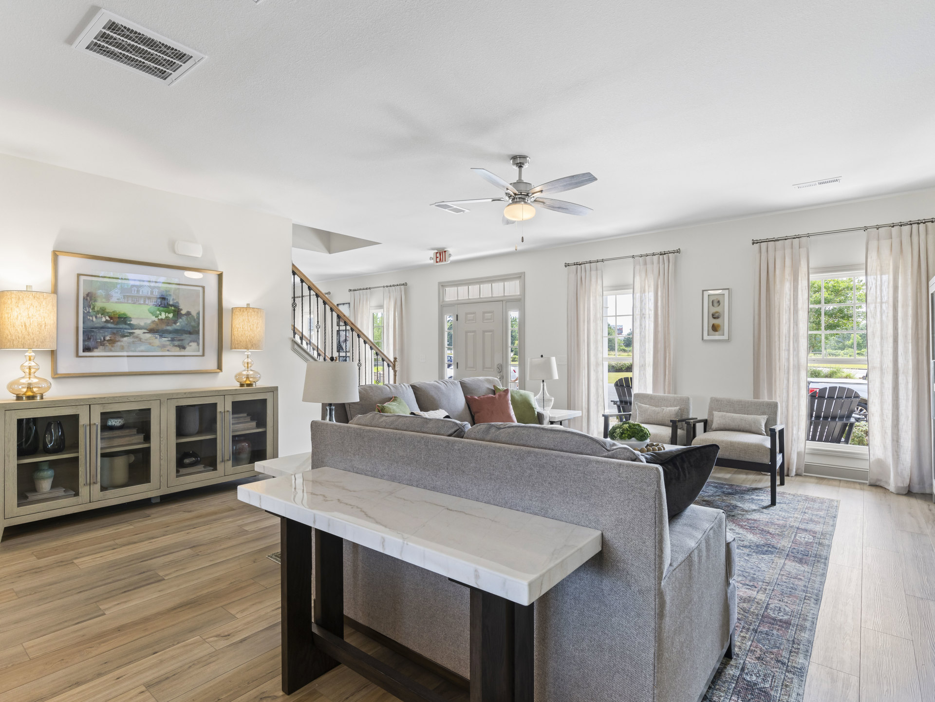 Living room with light gray couch, marble coffee table, framed house artwork on wall, glass cabinet with glass doors, and lamp with white shade