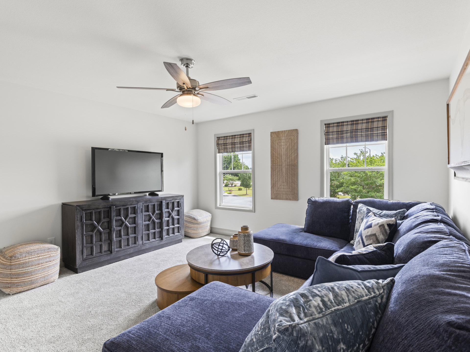 Living room with gray couch, TV on wooden stand, ceiling fan with light, coffee table holding decorative vase, pillow on floor, neutral walls and flooring