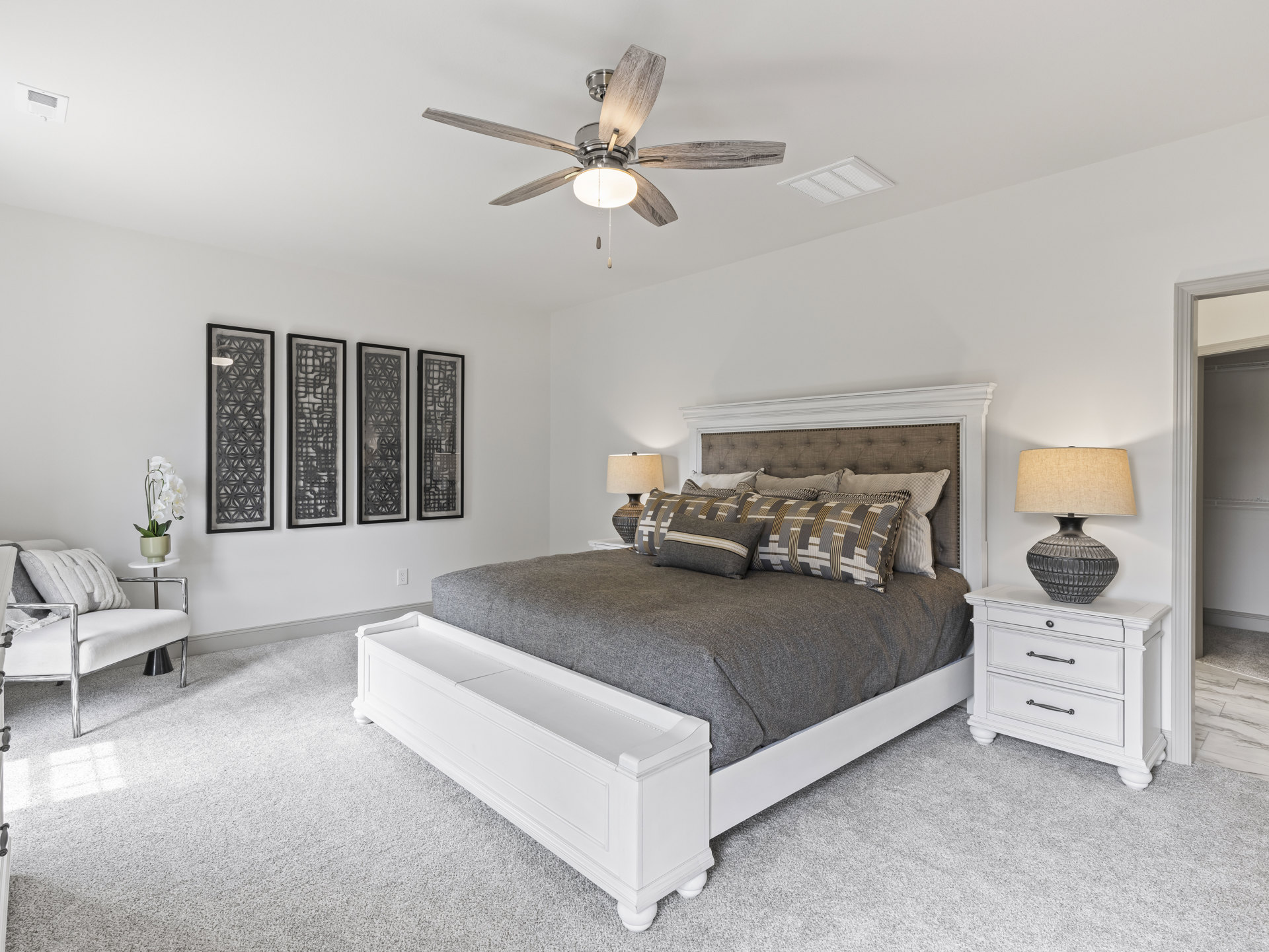 Bedroom with a ceiling fan, upholstered bed, bedside lamp, white couch with pillows, wall art arrangement, and a white orchid in a pot