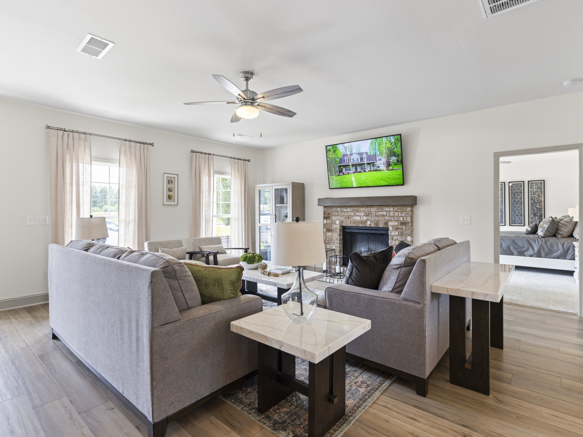 Spacious living room featuring neutral upholstered couches, stone fireplace with wood mantel, marble coffee table topped with glass vase, ceiling fan with integrated light