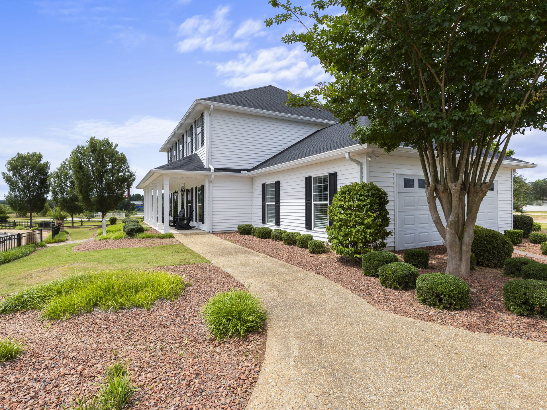 White house with white-framed windows, green leafy tree and bush in front, stone path leading through landscaped yard