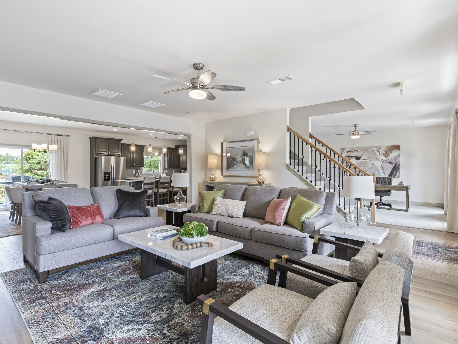 Living room with light-colored couches, pink and patterned pillows, wooden coffee table holding a bowl of green plants and a book, neutral walls, and hardwood flooring